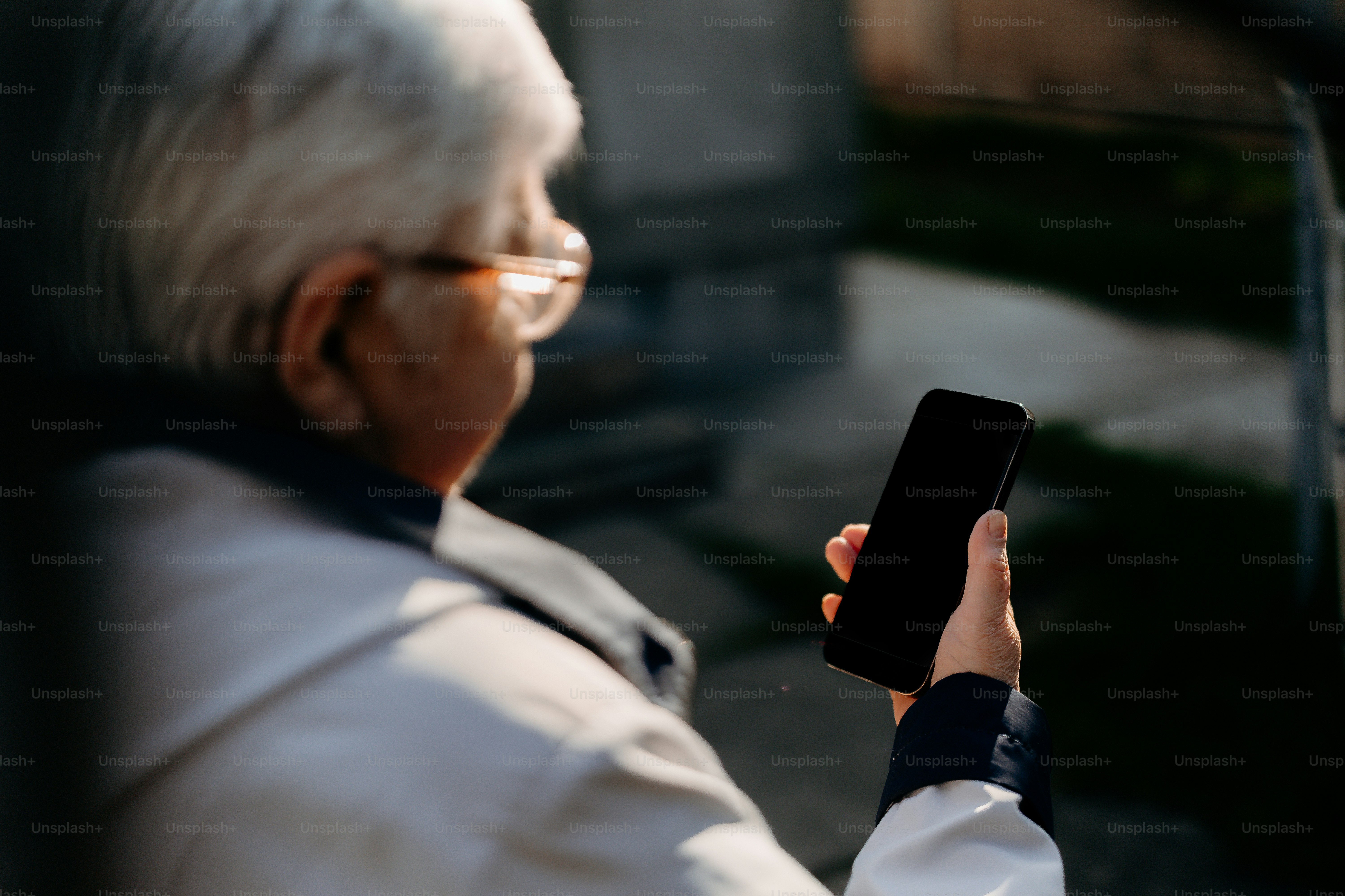 Elderly person holding a smartphone outdoors.