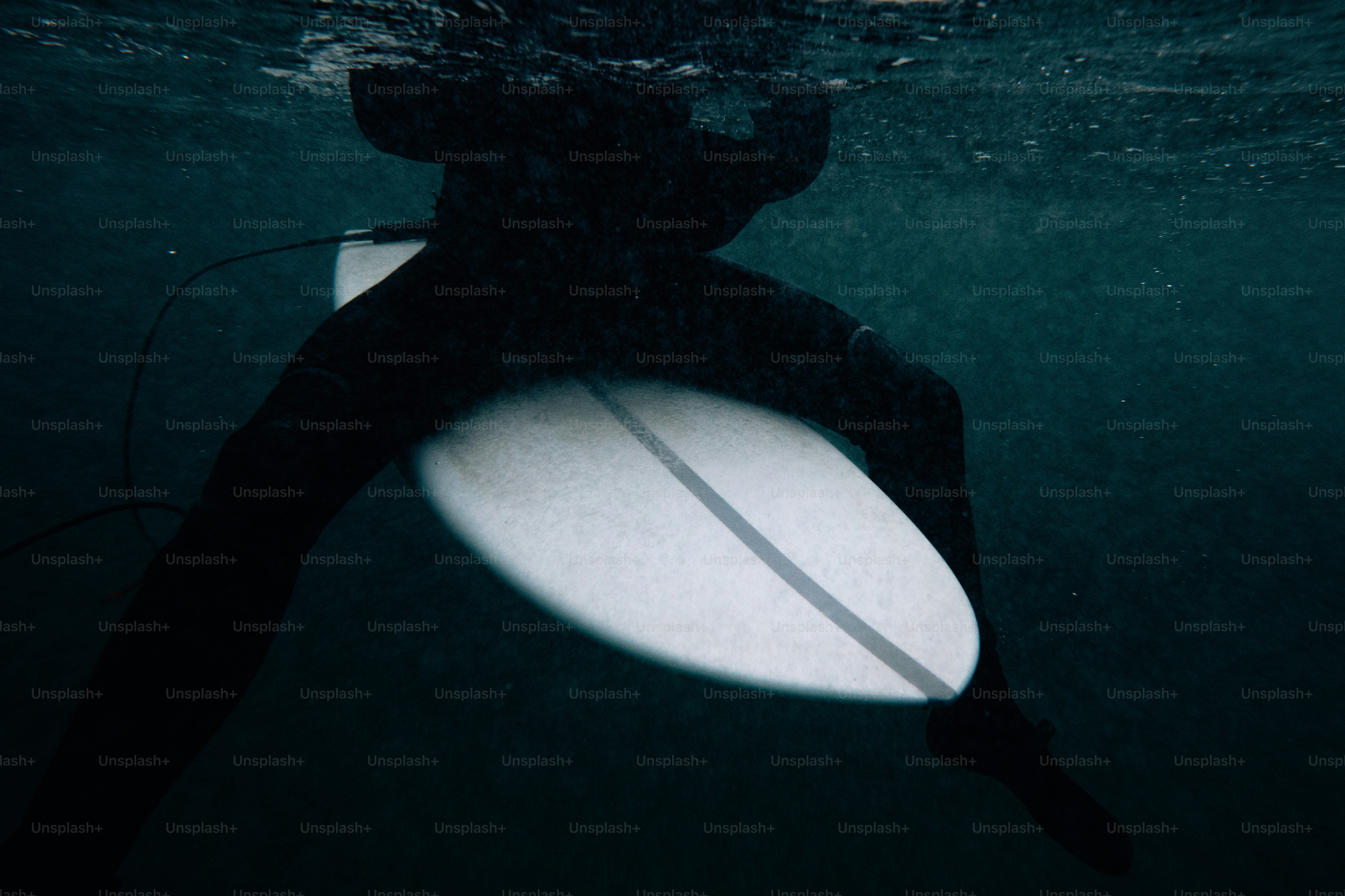 Surfista in muta che tiene la tavola da surf sott'acqua