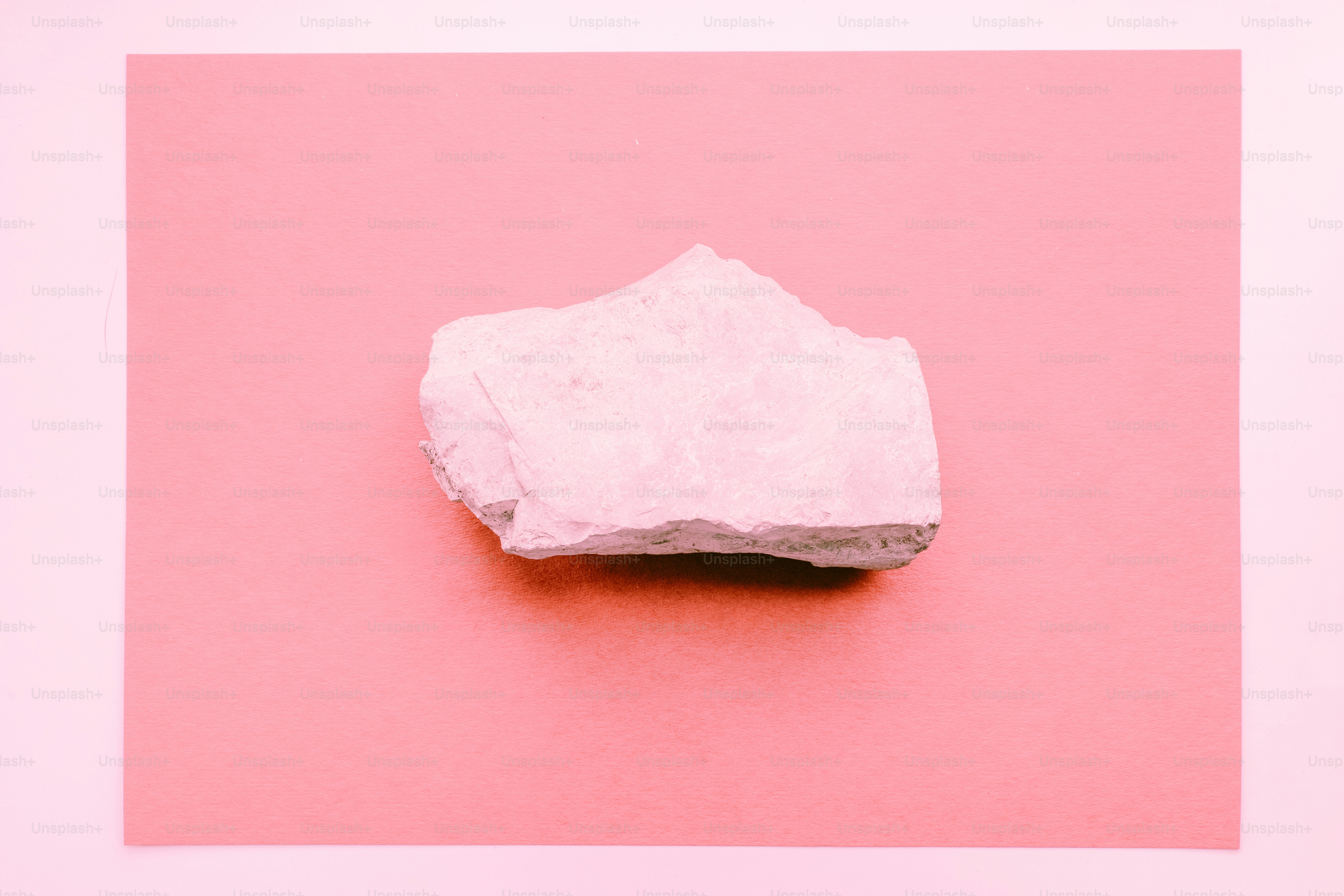 A light pink rock rests on a pink background.