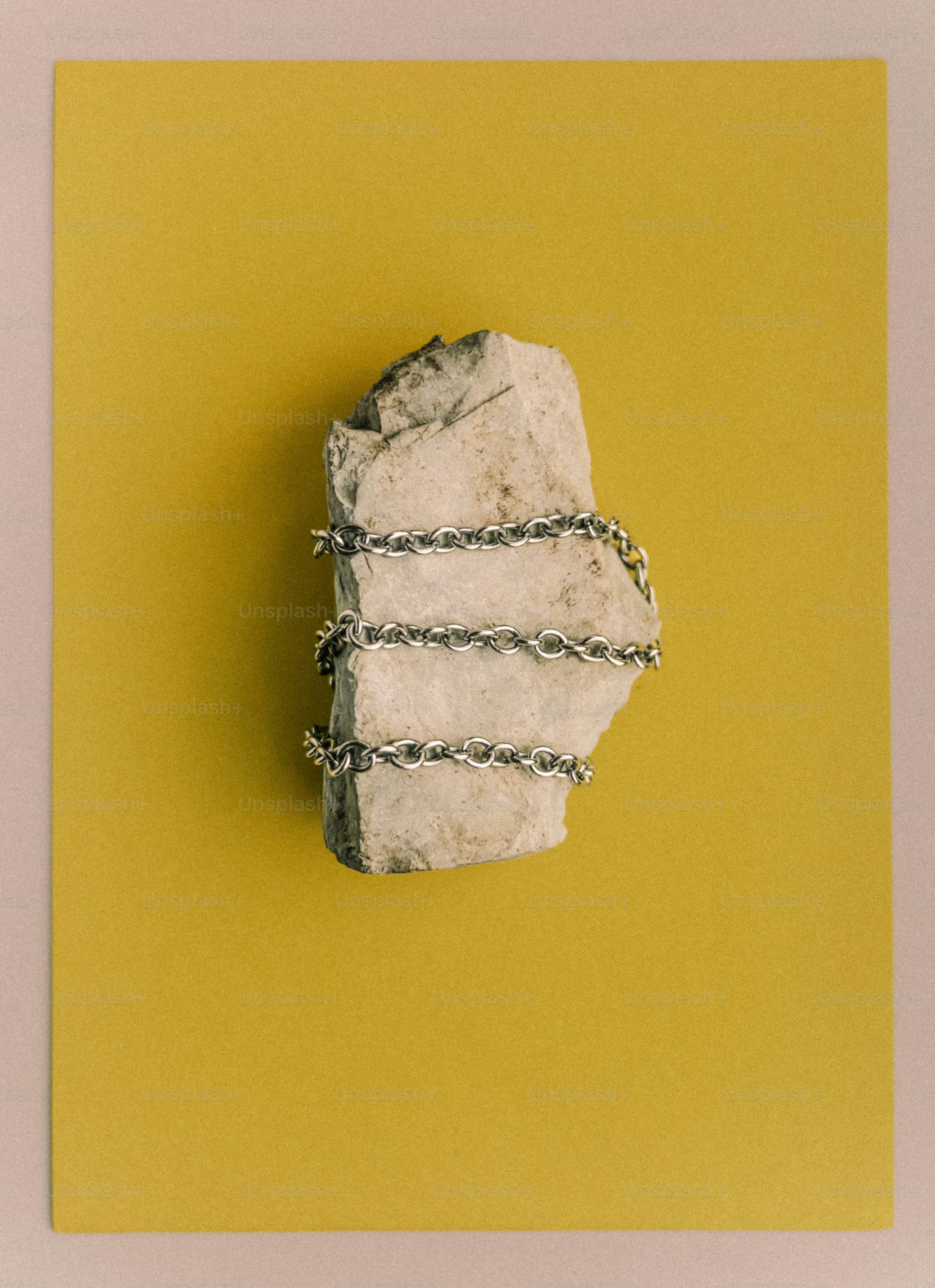 A stone wrapped in silver chain on yellow background