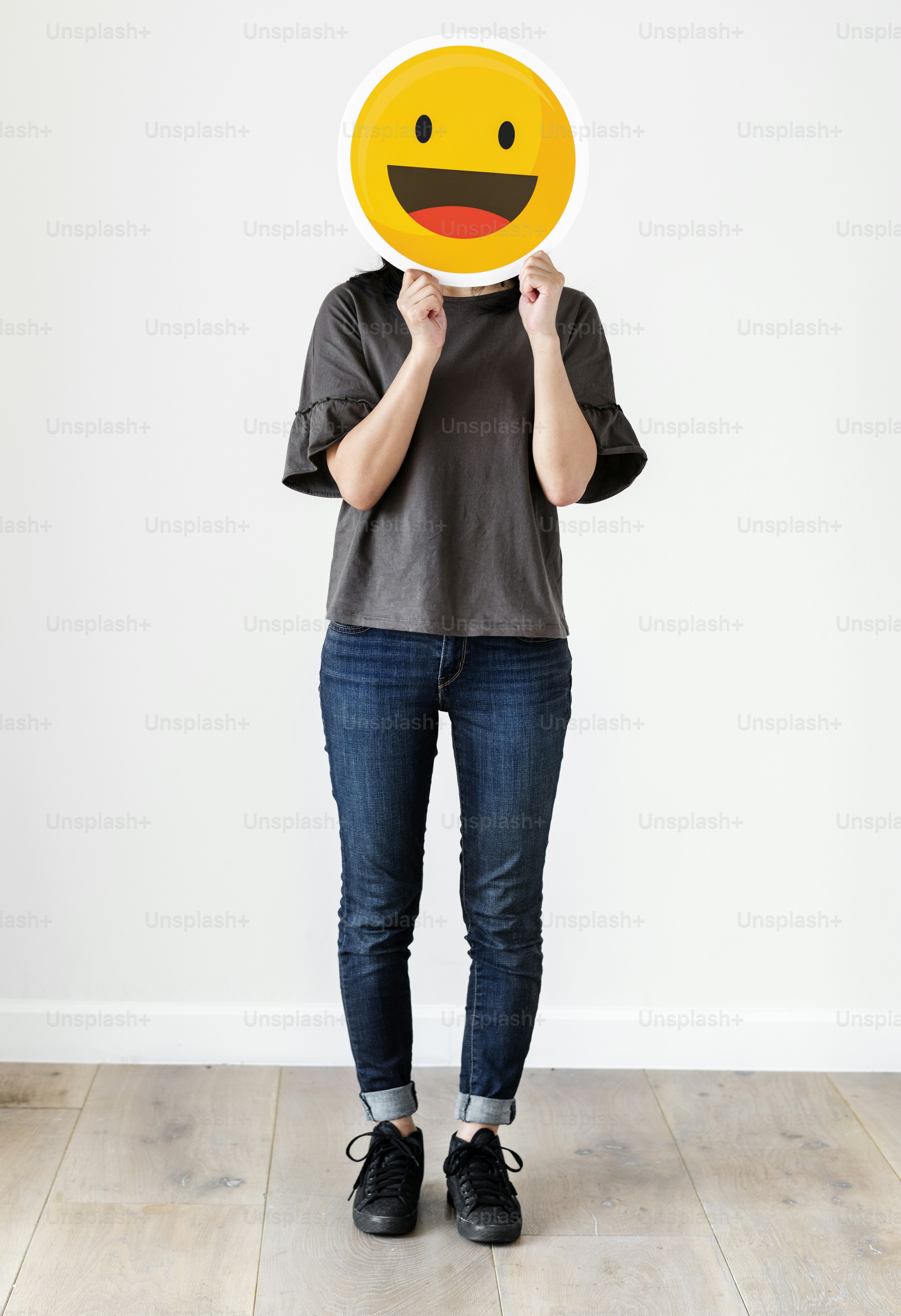 Eine Person in einem grauen T-Shirt und Jeans hält ein großes, lächelndes Emoji-Schild