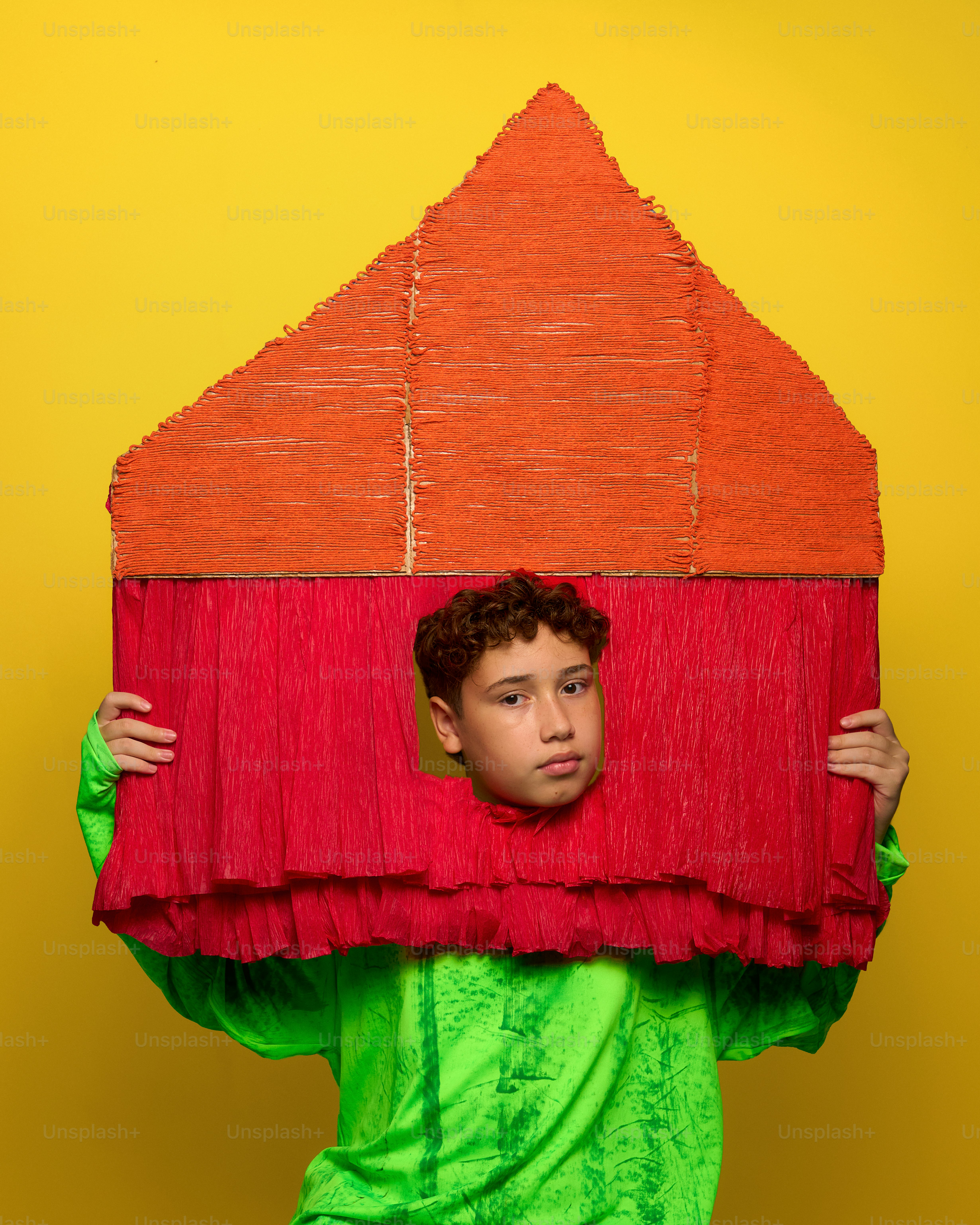 A boy peeks through a colorful, handmade house prop.