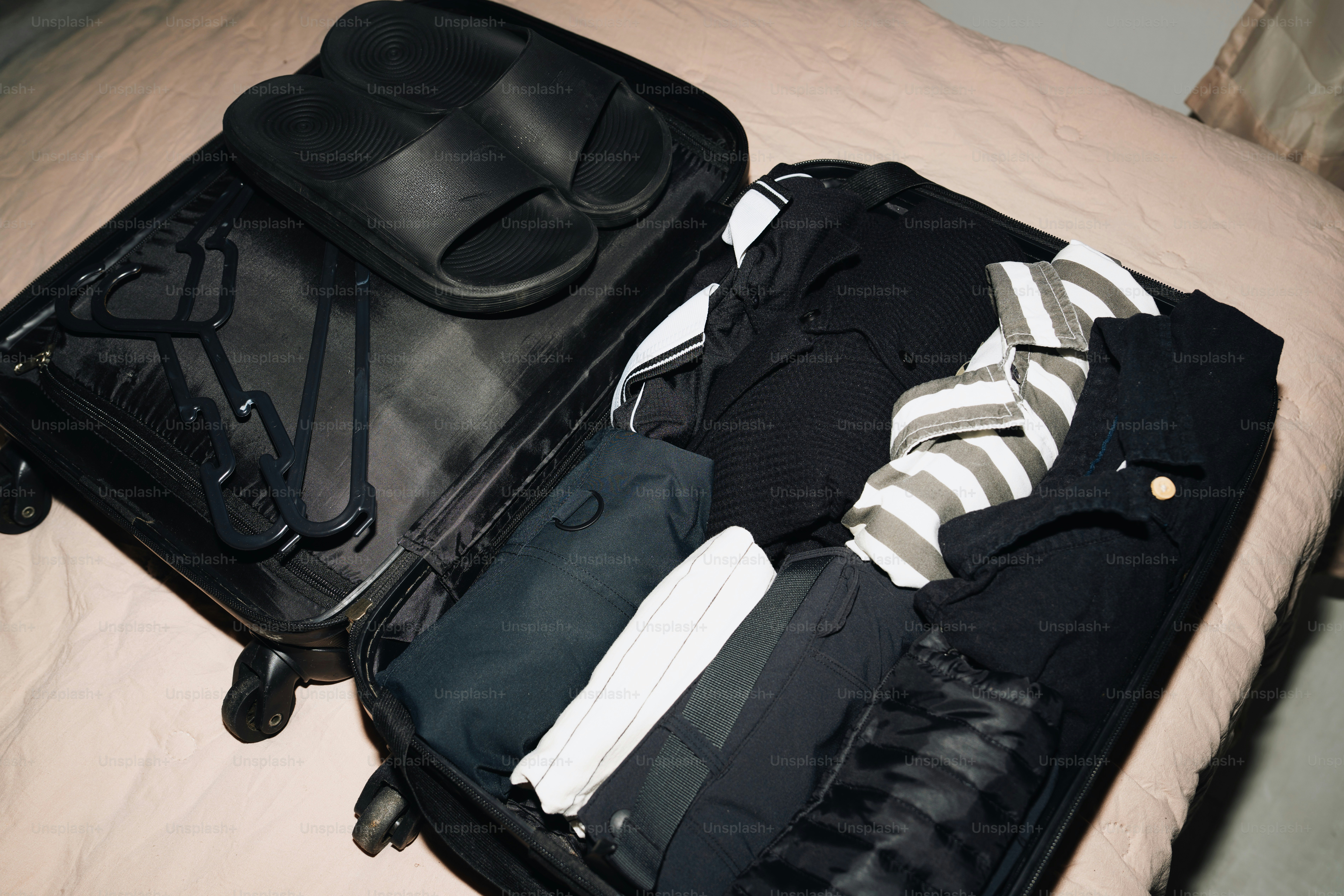 Suitcase packed with clothes and sandals on bed