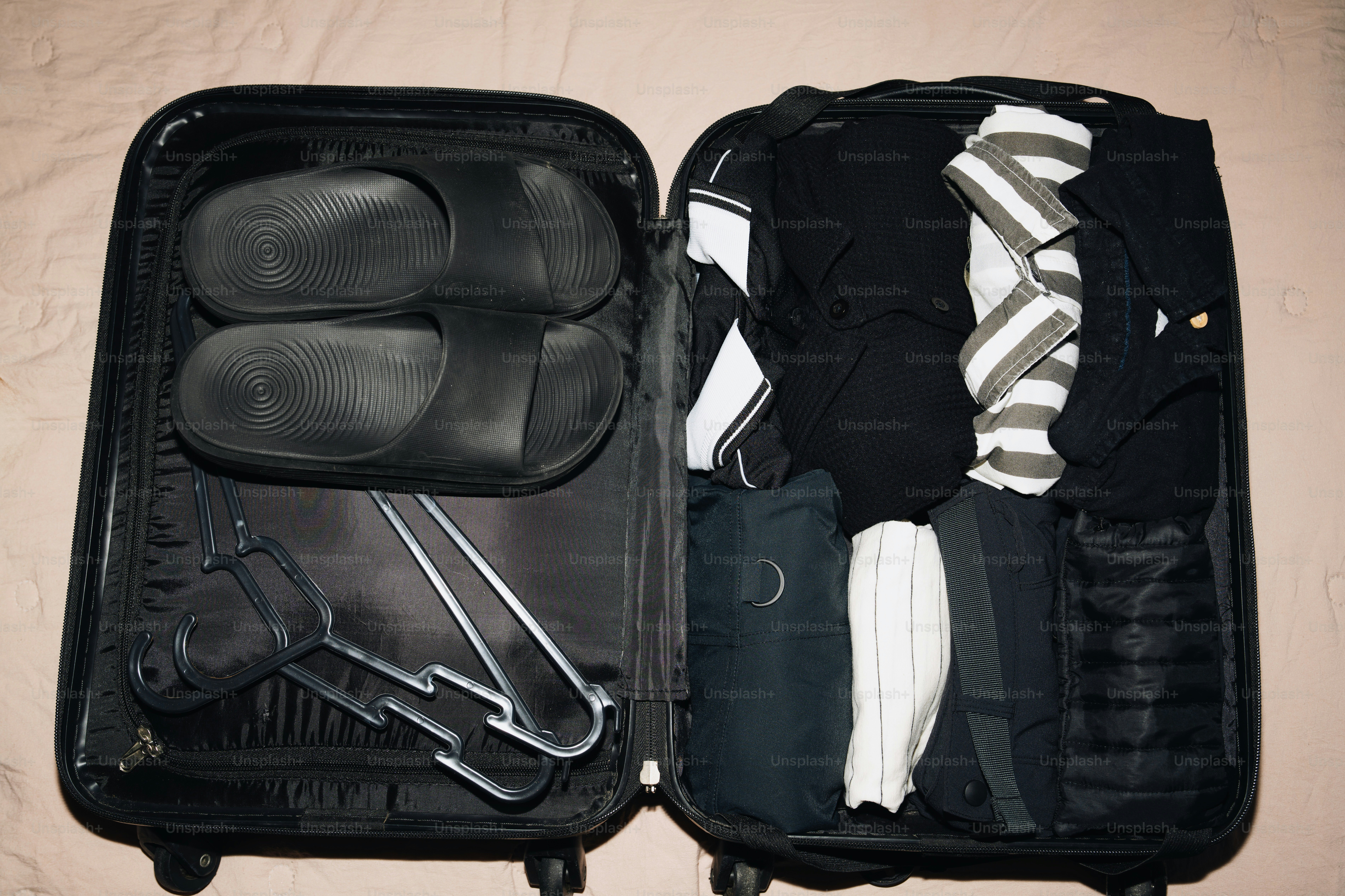 Open suitcase packed with clothes and sandals.