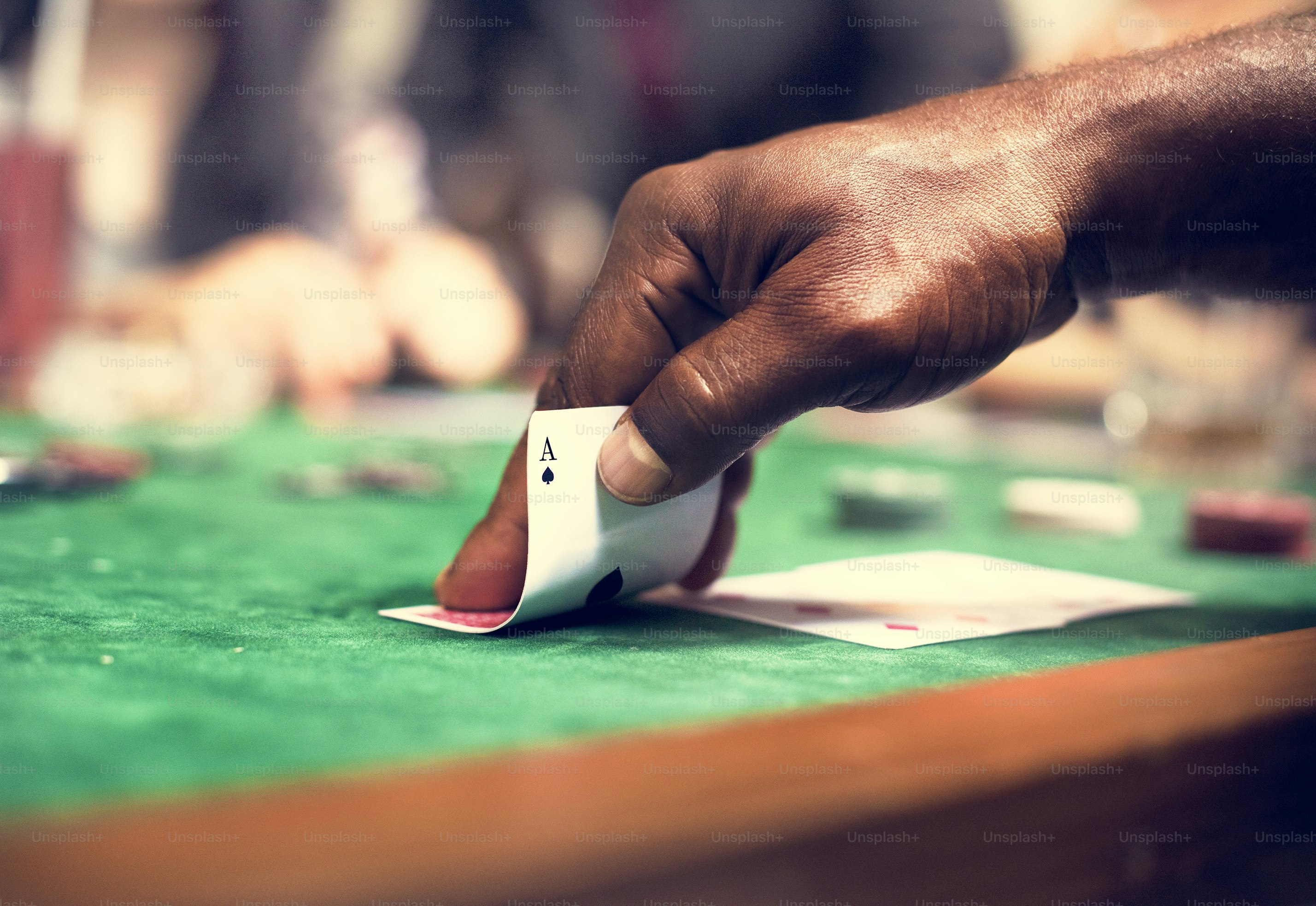 A hand holding an ace of spades playing card on a green felt table