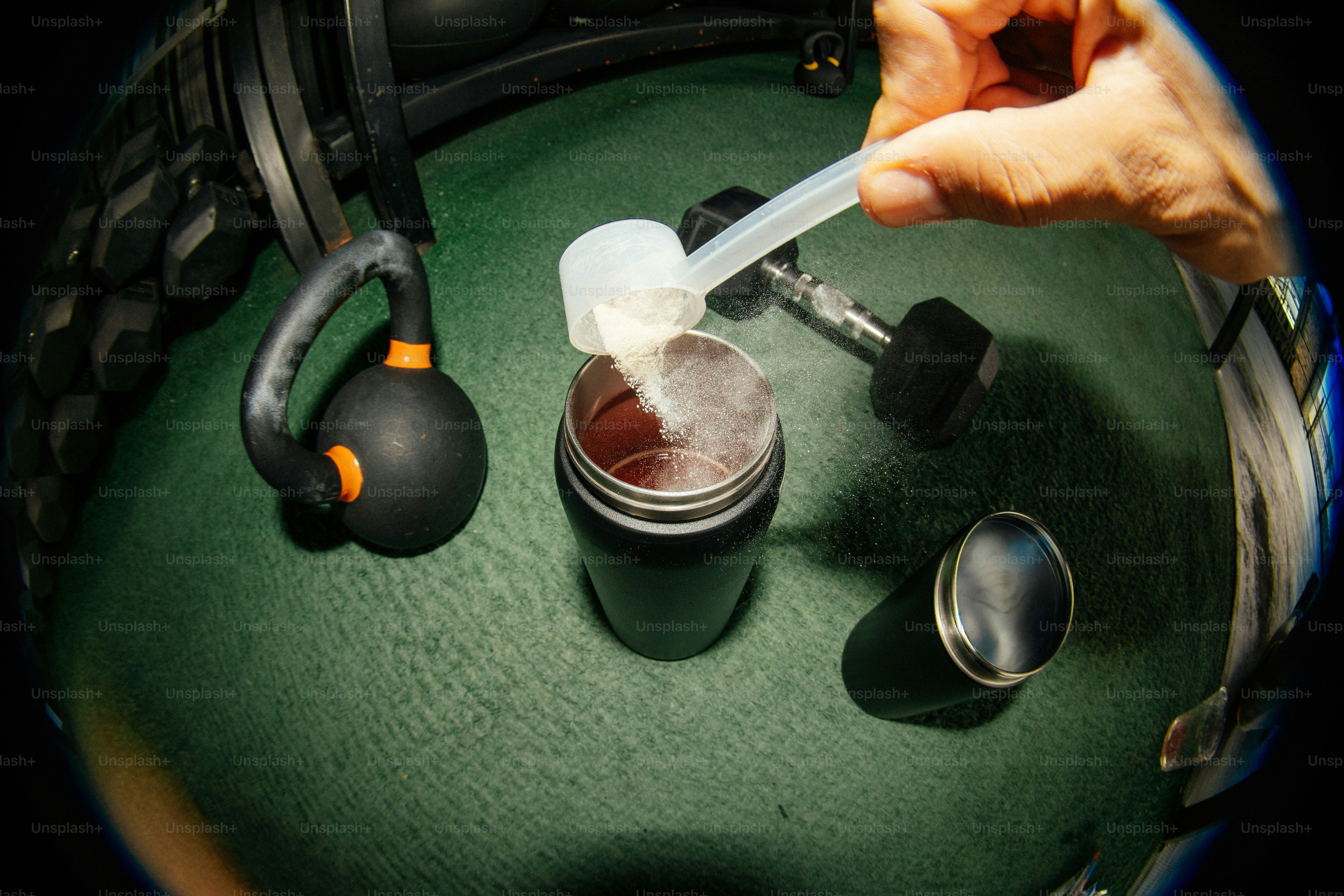 Hand adds protein powder to a shaker bottle with weights.