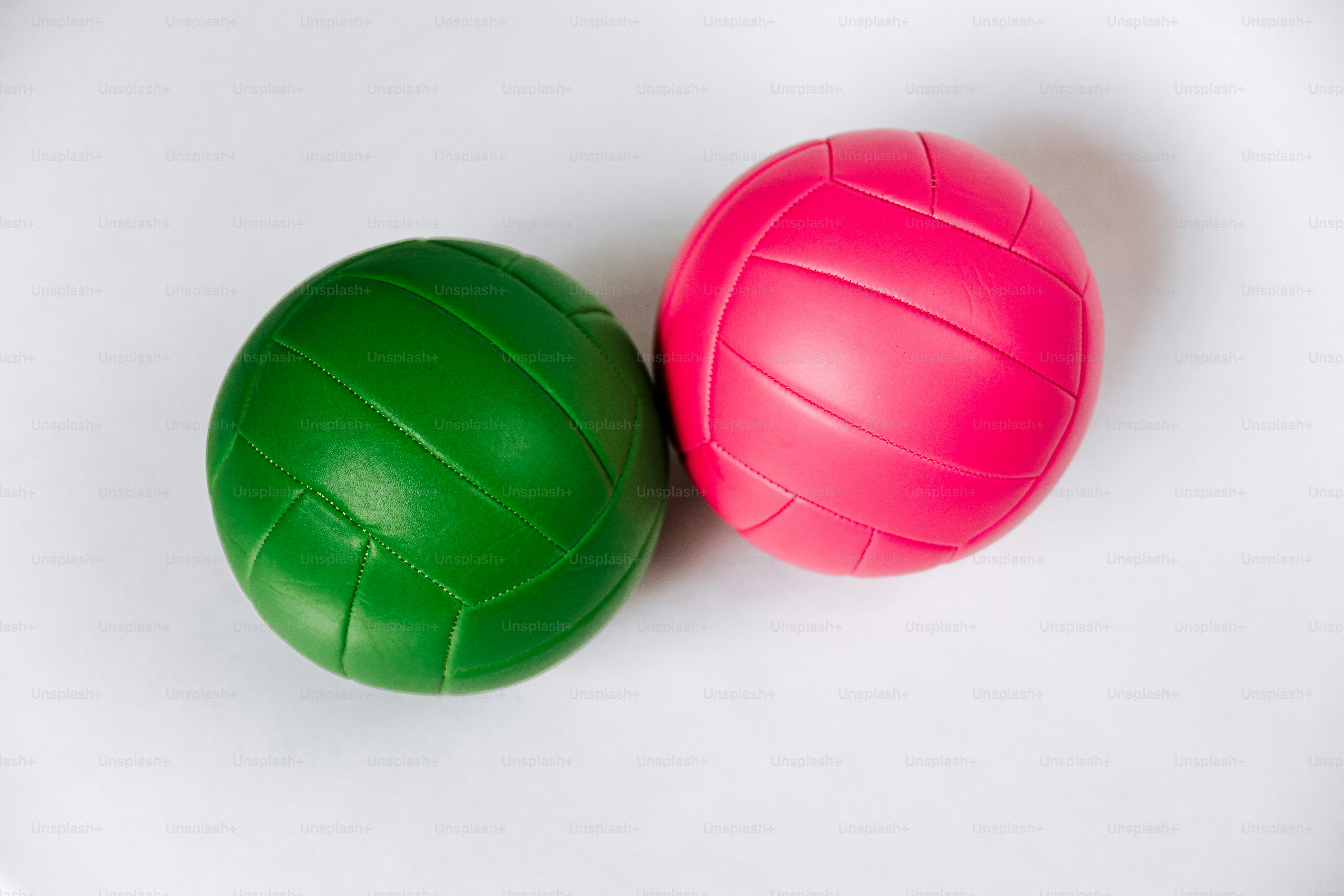 Zwei Volleybälle, einer grün und einer pink, auf weißer Oberfläche