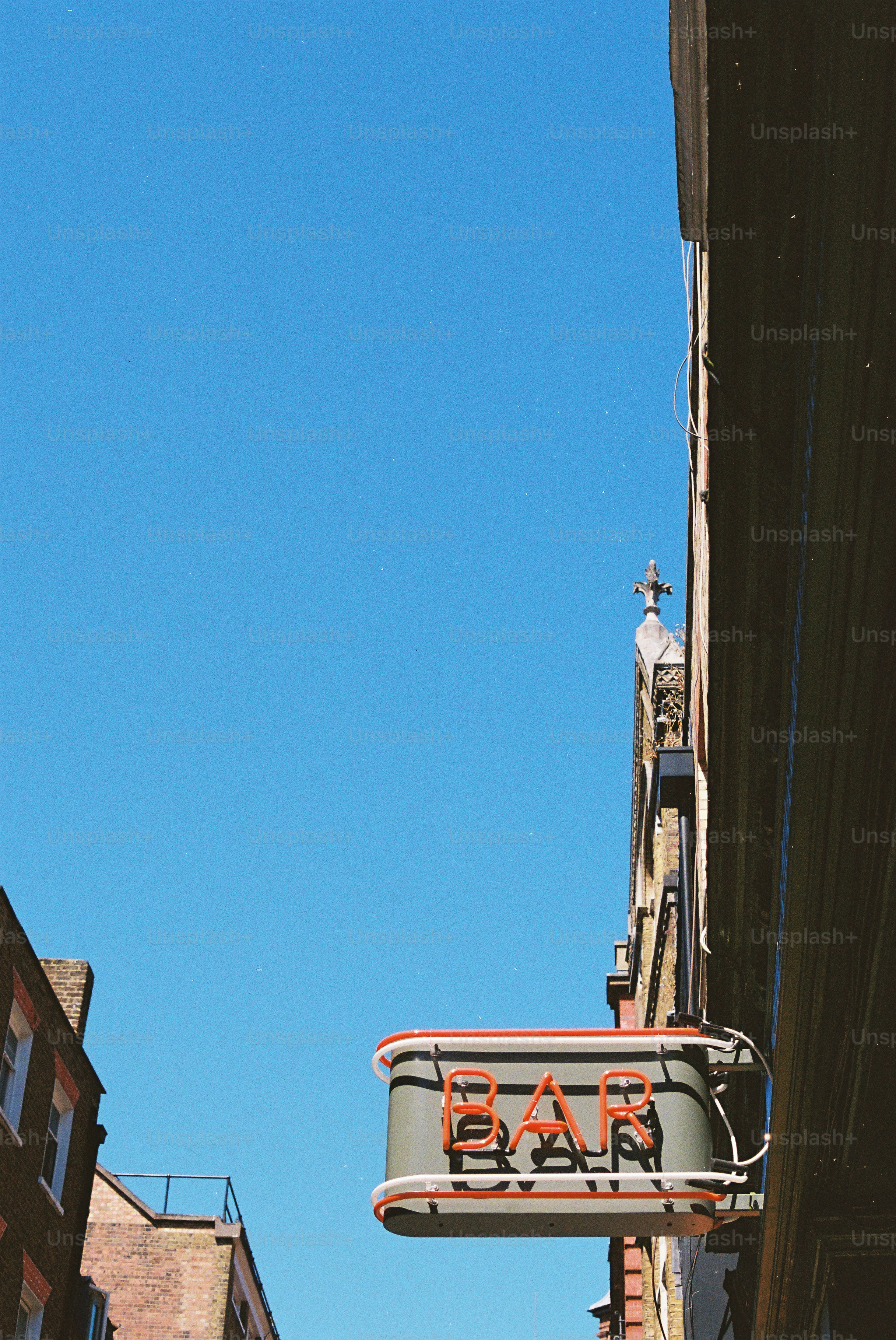 A neon bar sign against a clear blue sky.