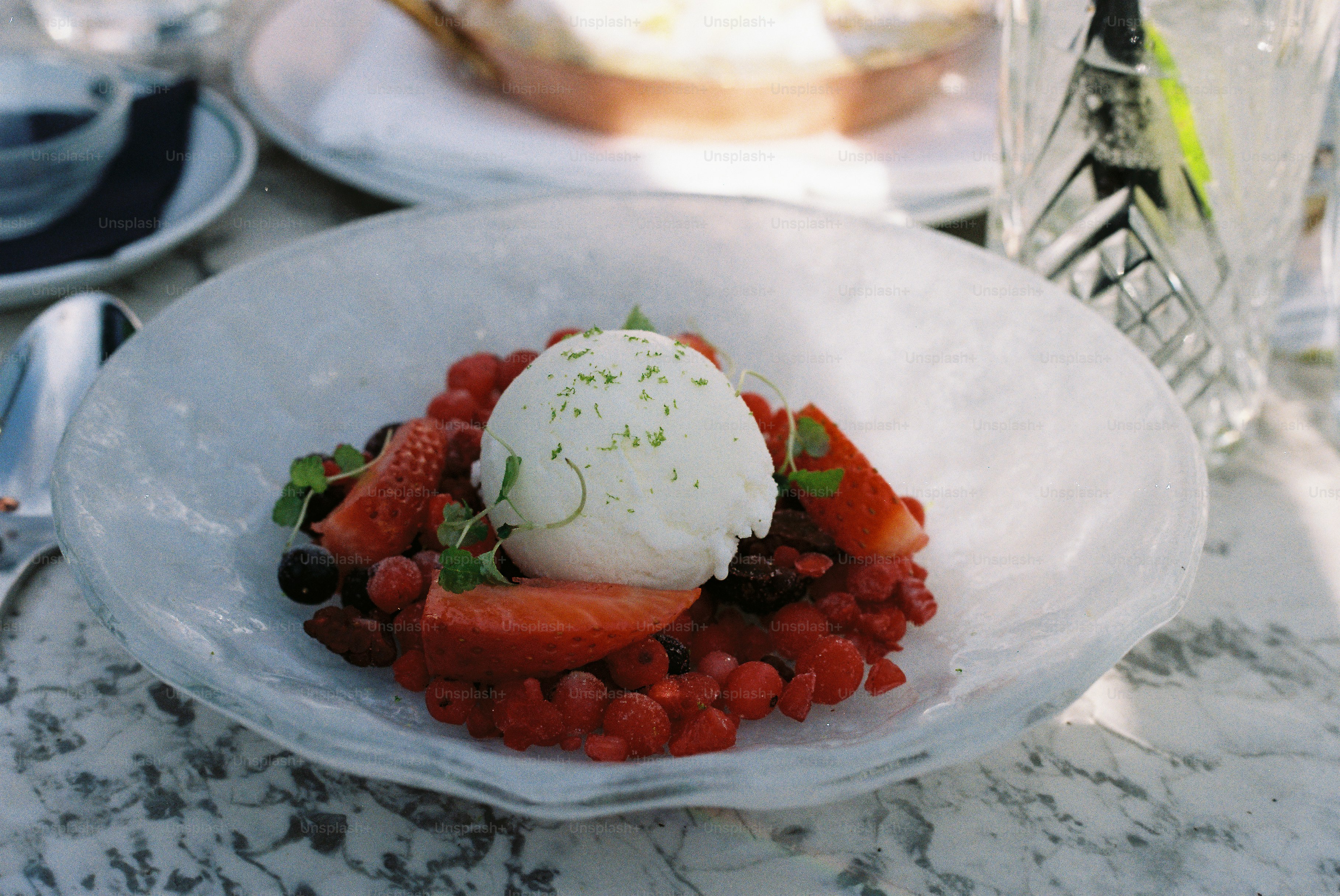 A bowl of berries topped with ice cream and mint.