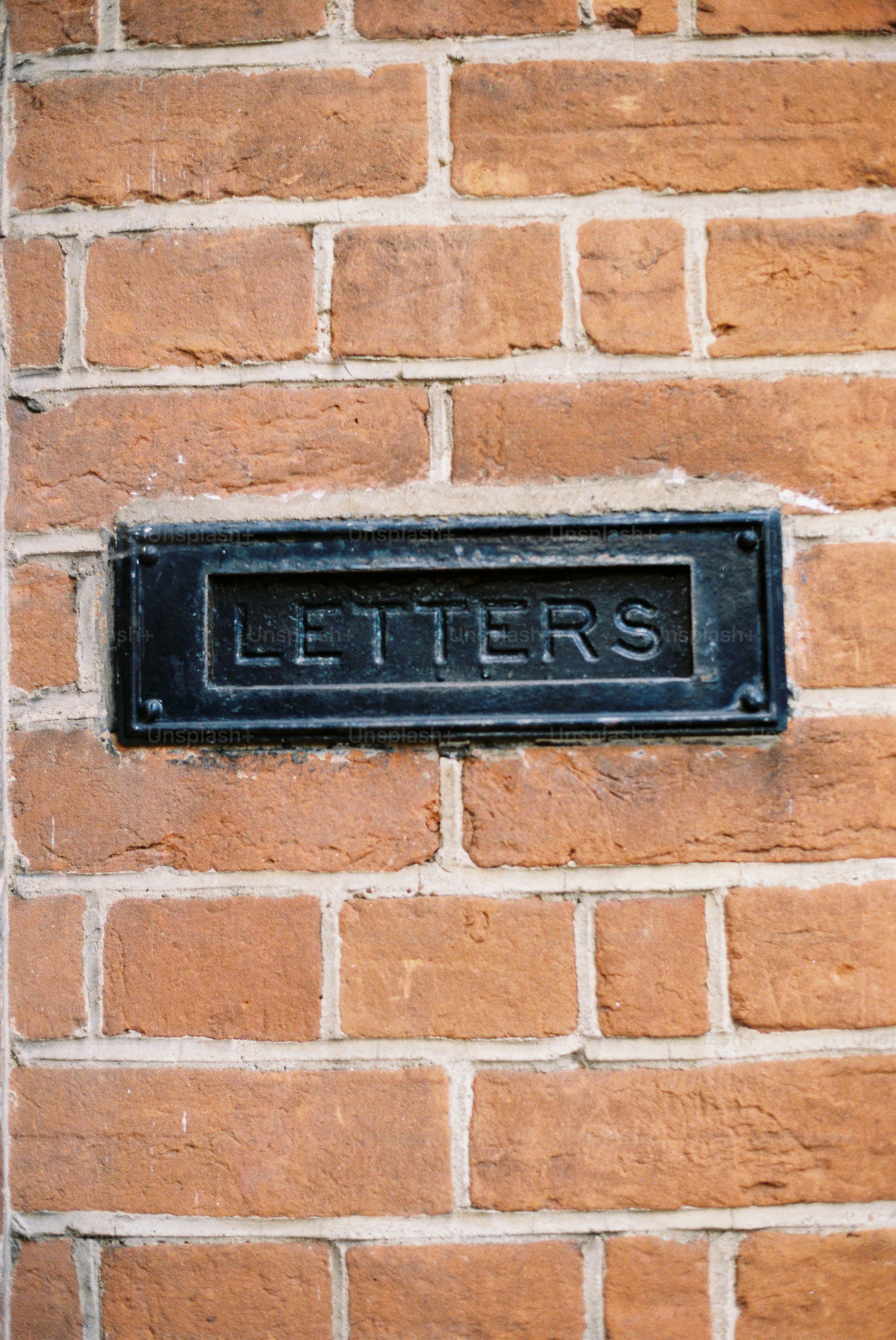 A black metal mailbox slot on a brick wall