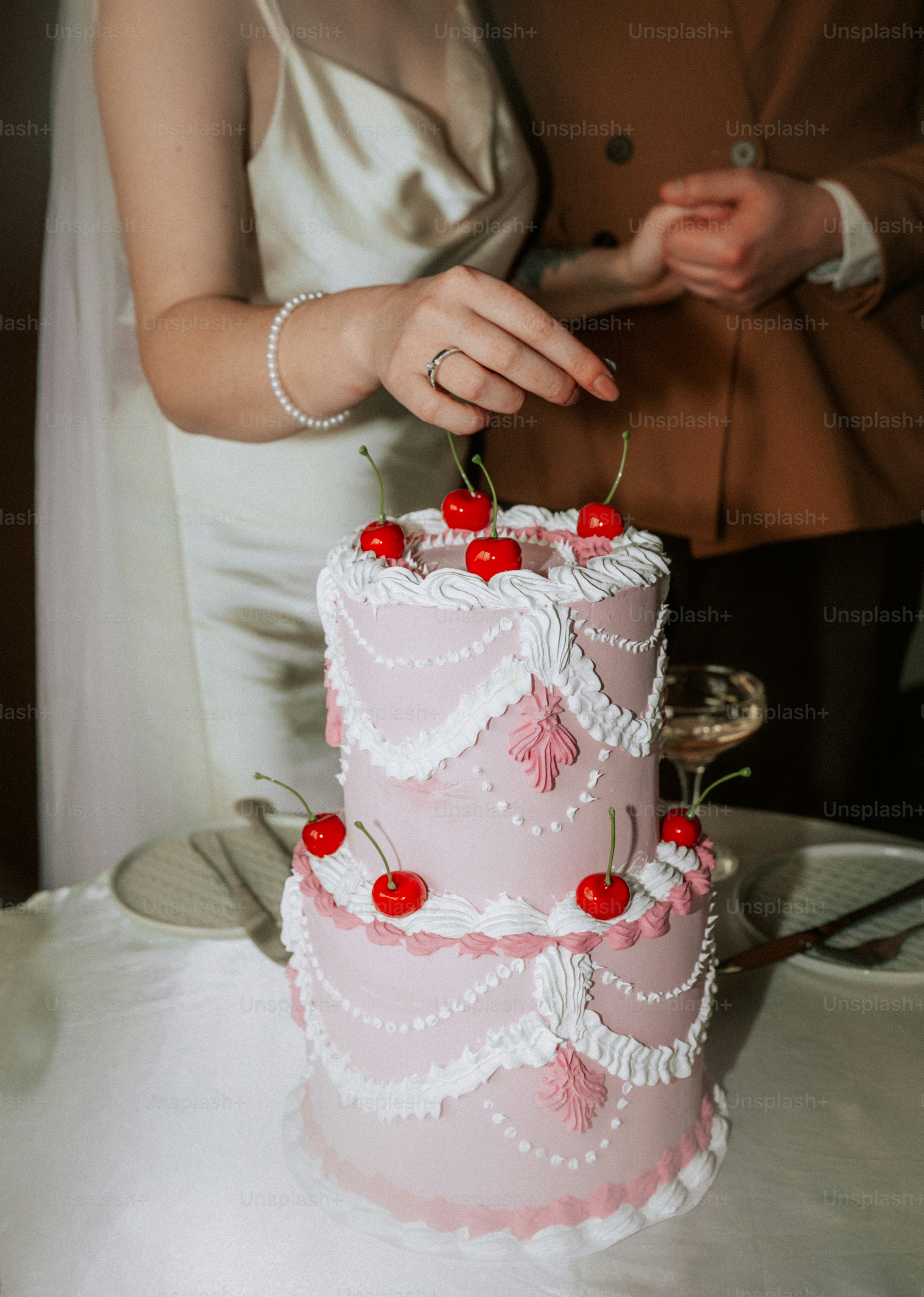 A couple cuts a pink two-tiered wedding cake with cherries.