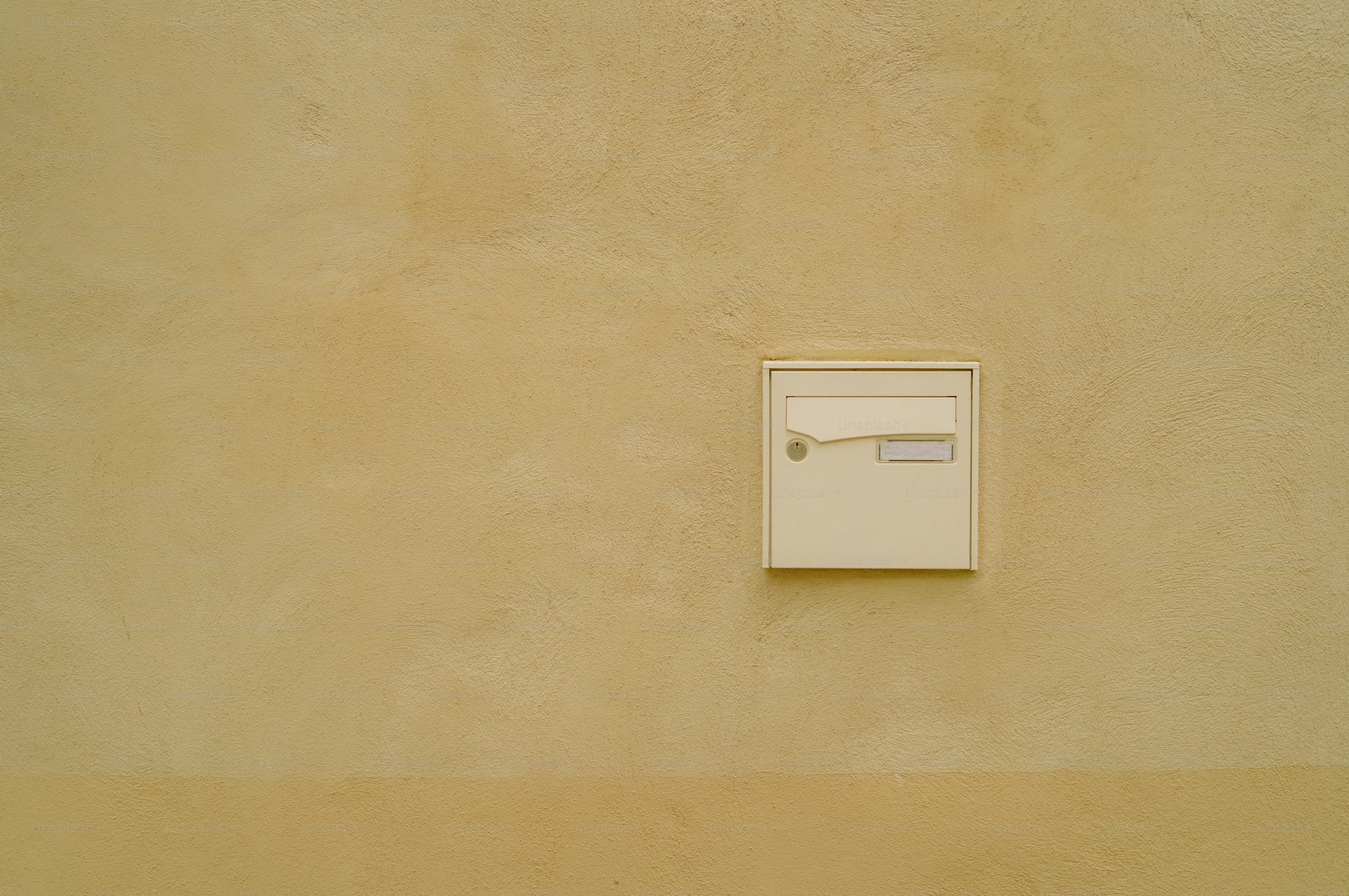 A small white mailbox on a textured yellow wall