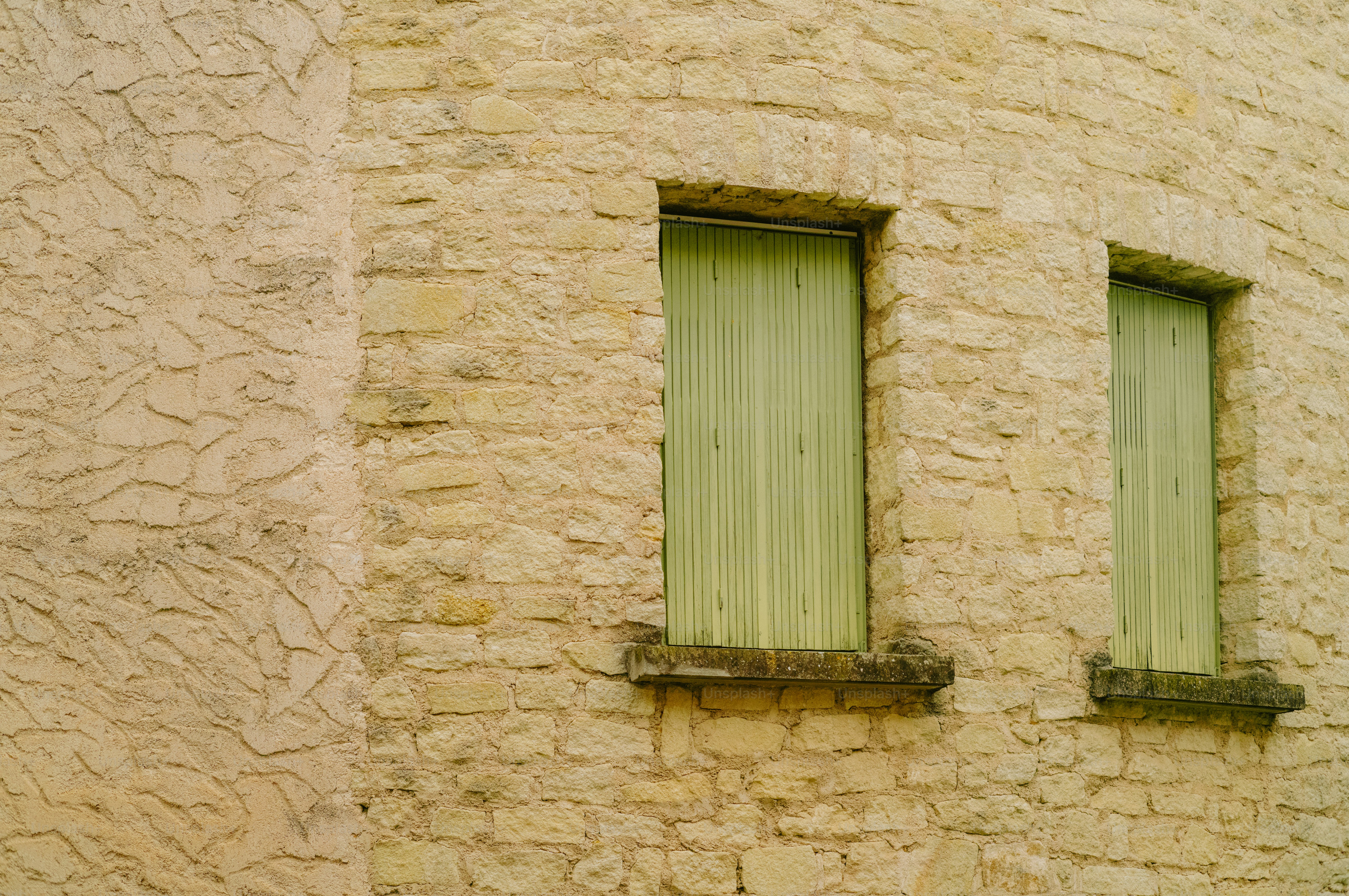 Two windows with green shutters on a textured wall