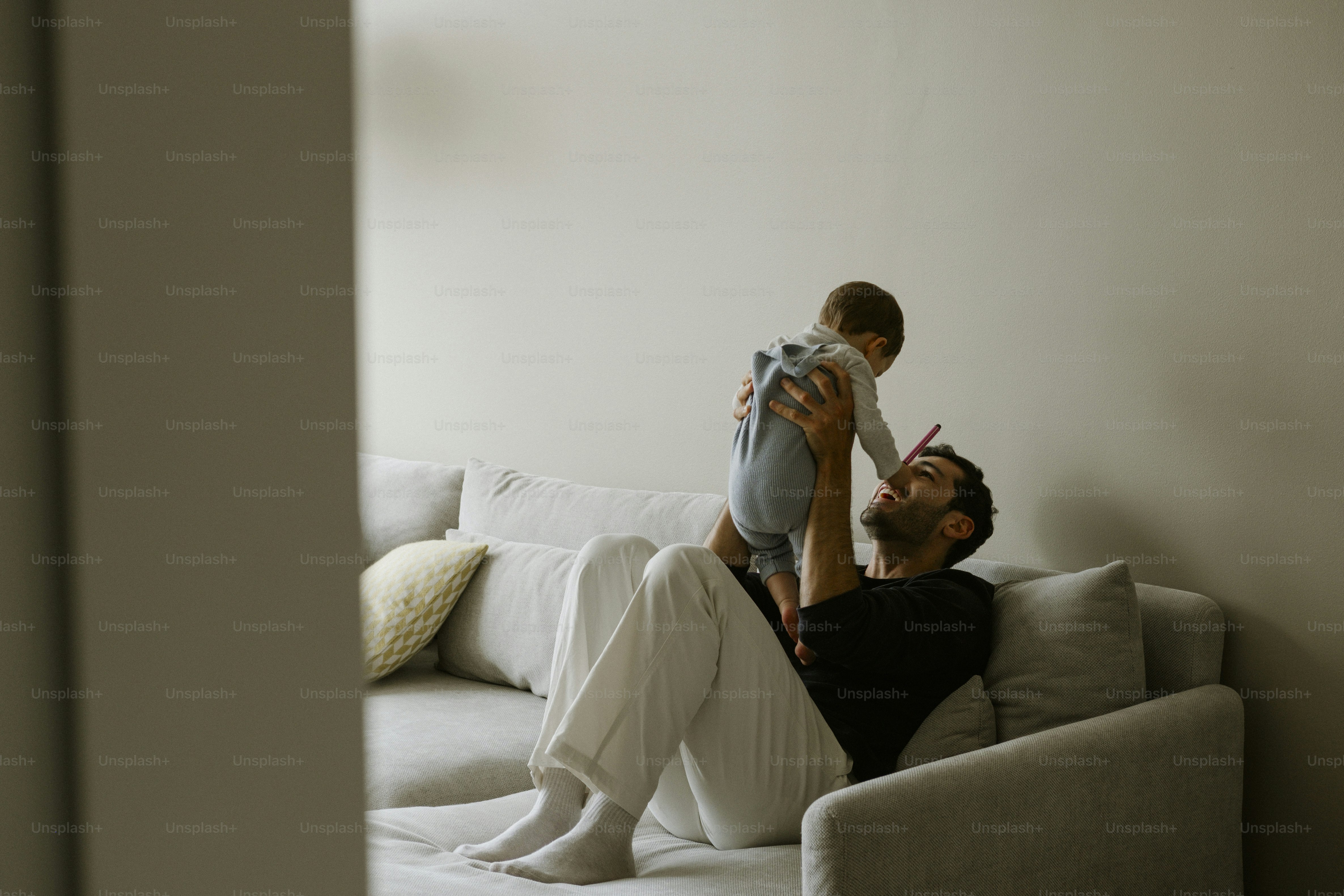 Padre levantando a su hijo pequeño en el aire en el sofá
