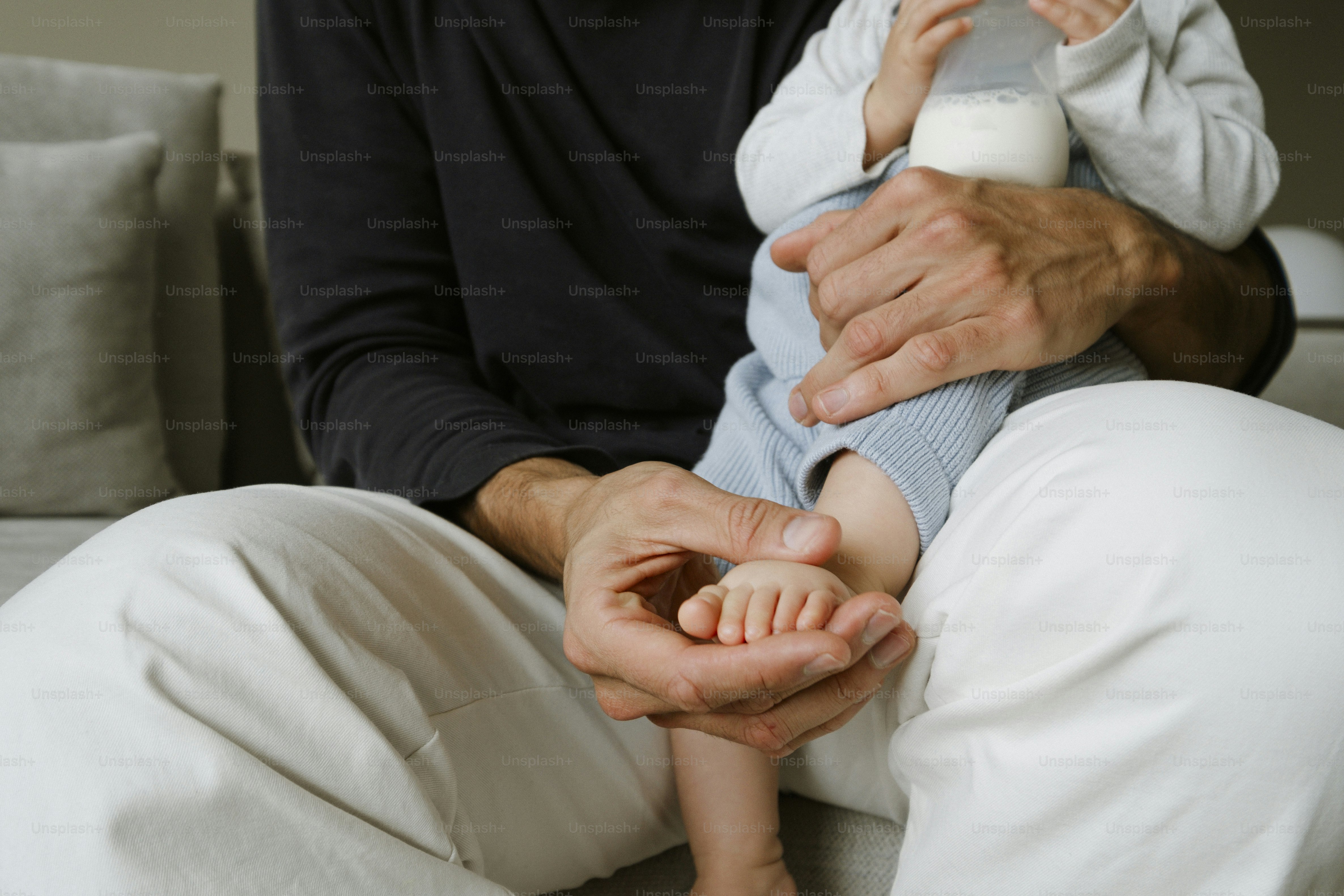 Father feeding baby with milk bottle on couch
