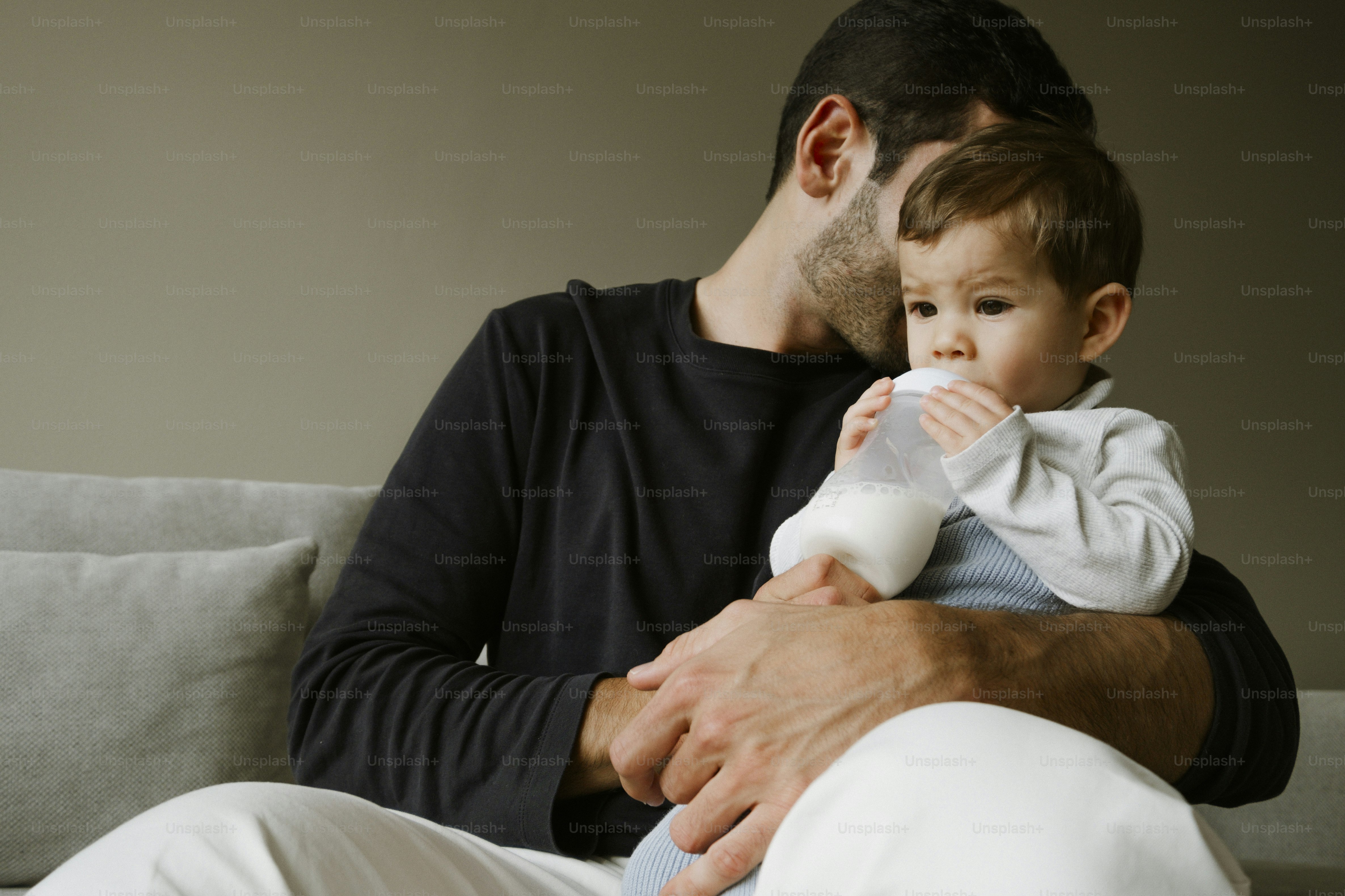 Father feeding baby milk from a bottle on the couch.