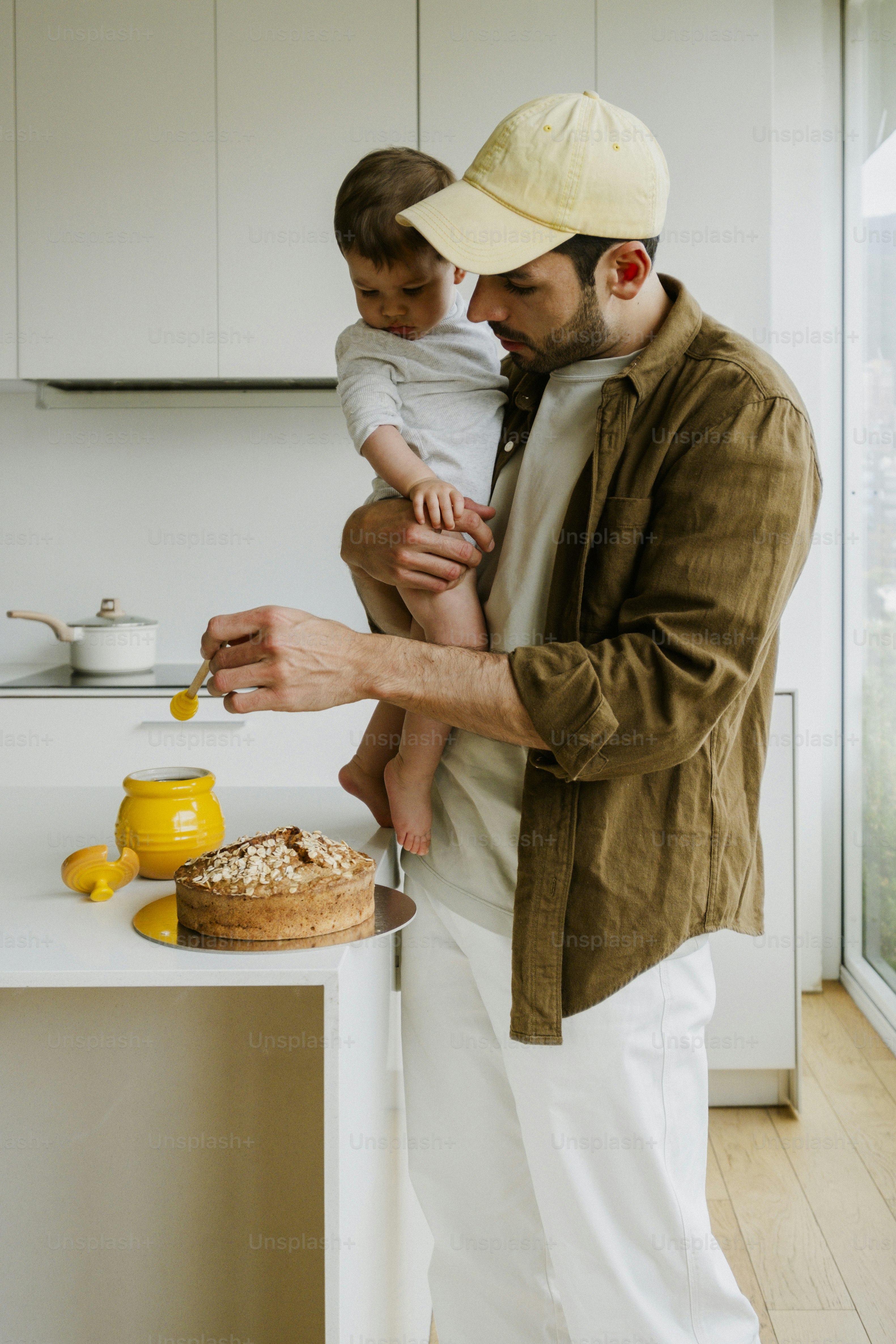 Father holding baby while decorating cake in kitchen