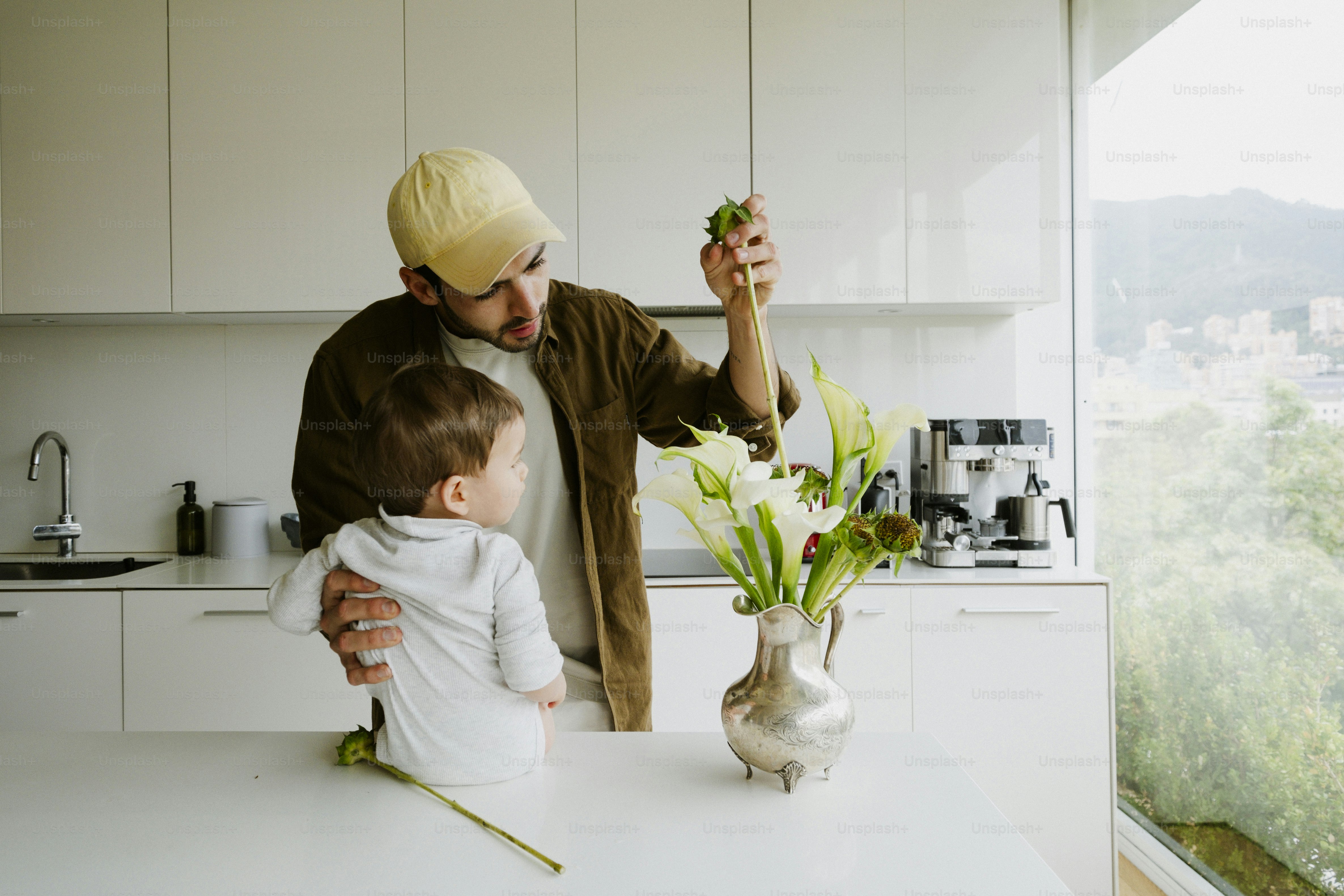 Man shows a flower to a child in a kitchen.