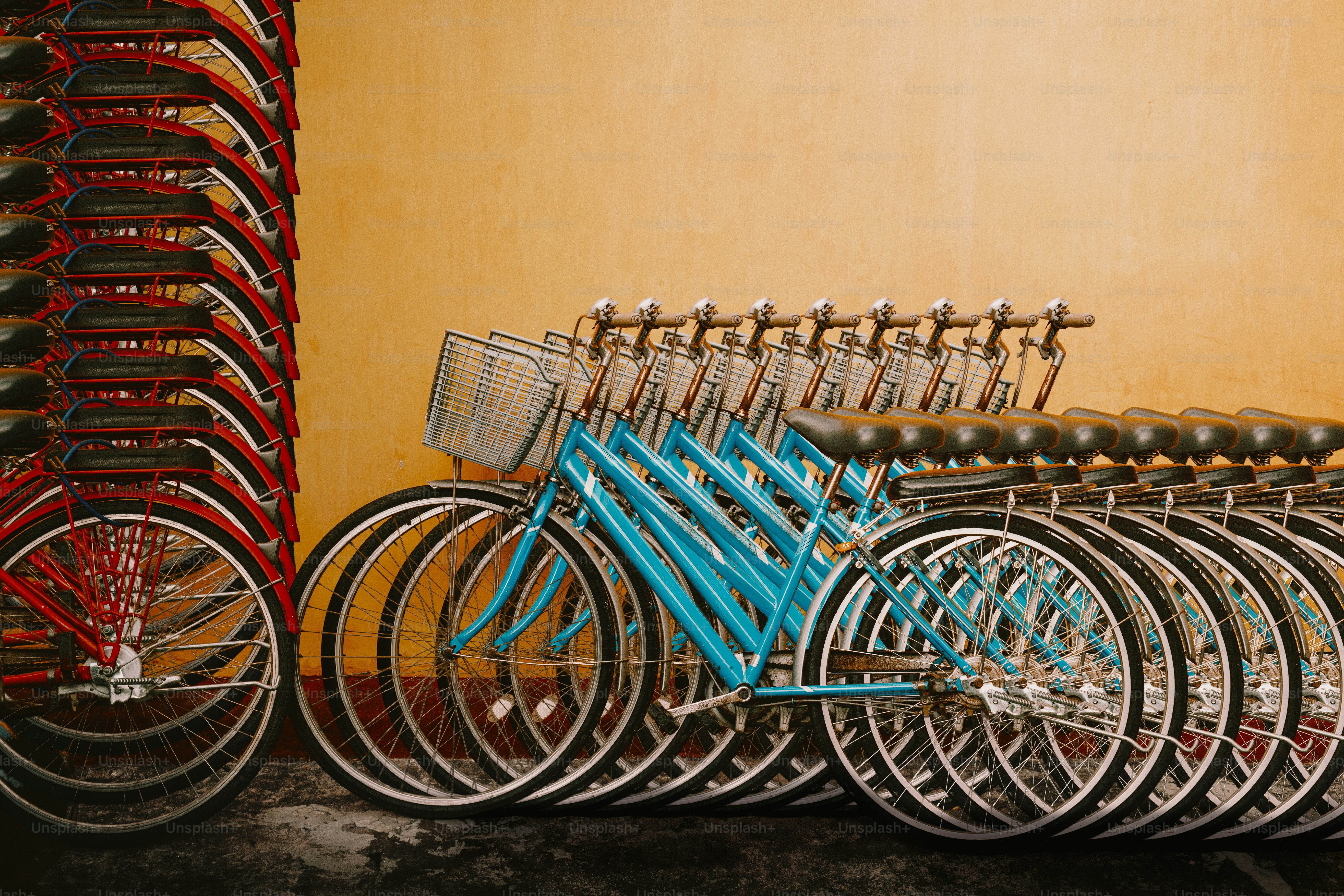 Many bicycles, red and blue, stacked against a yellow wall