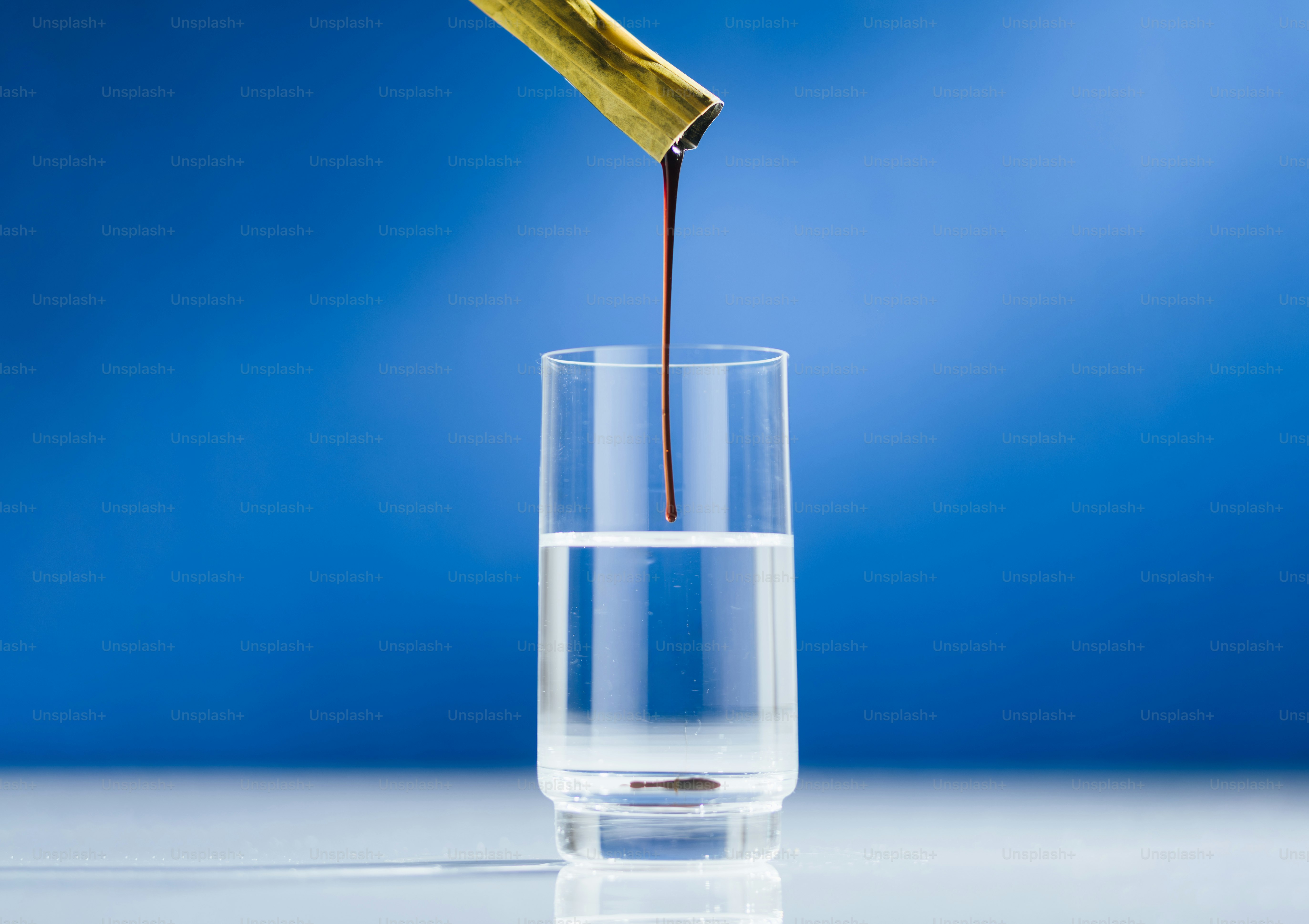 Goldene Tube tropft dunkle Flüssigkeit ins klare Glas