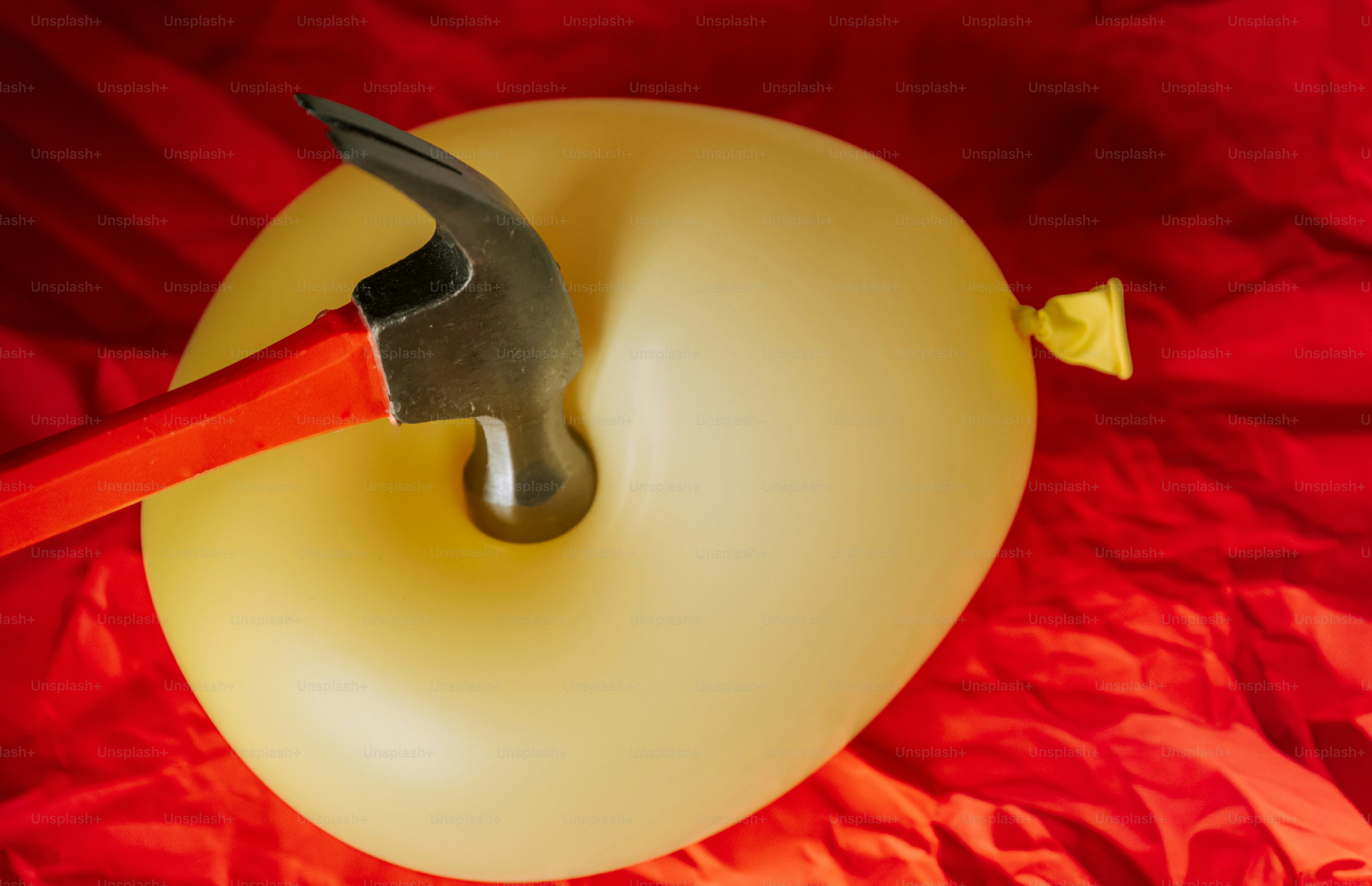 Hammer striking a yellow balloon on red background