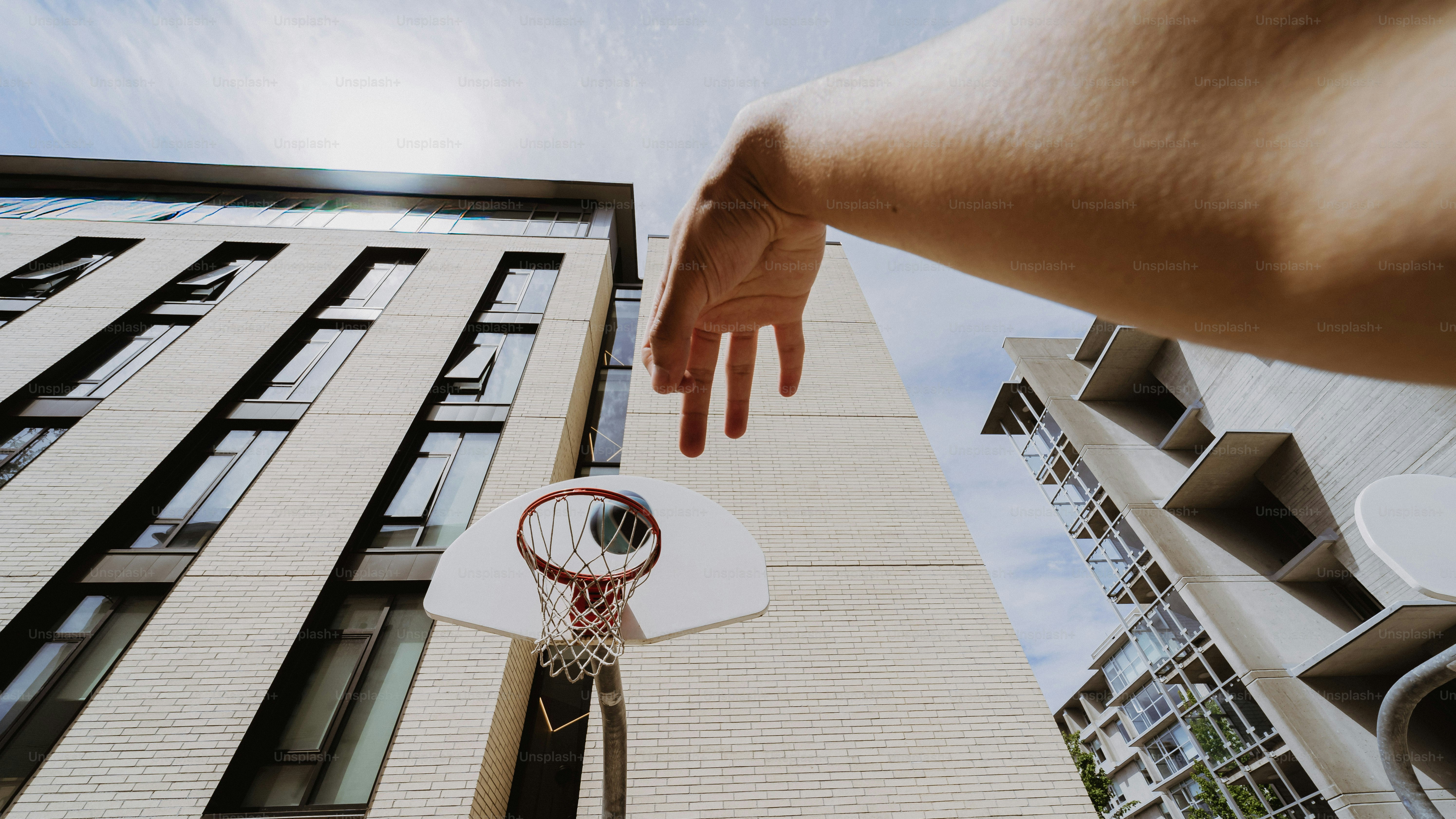 Person reaching for a basketball hoop on a building