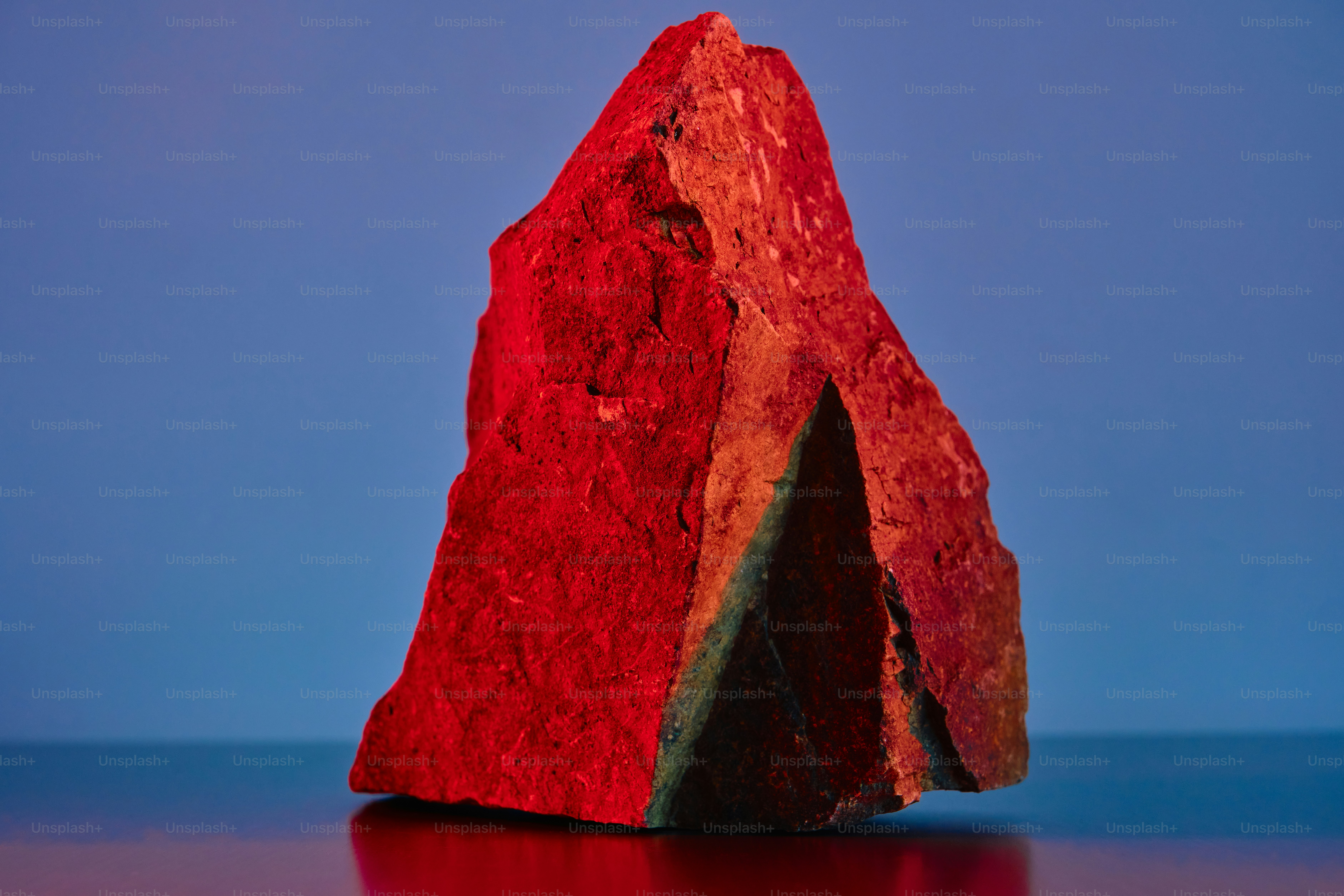 A rough red stone against a blue background photo – Minimalist Image on ...