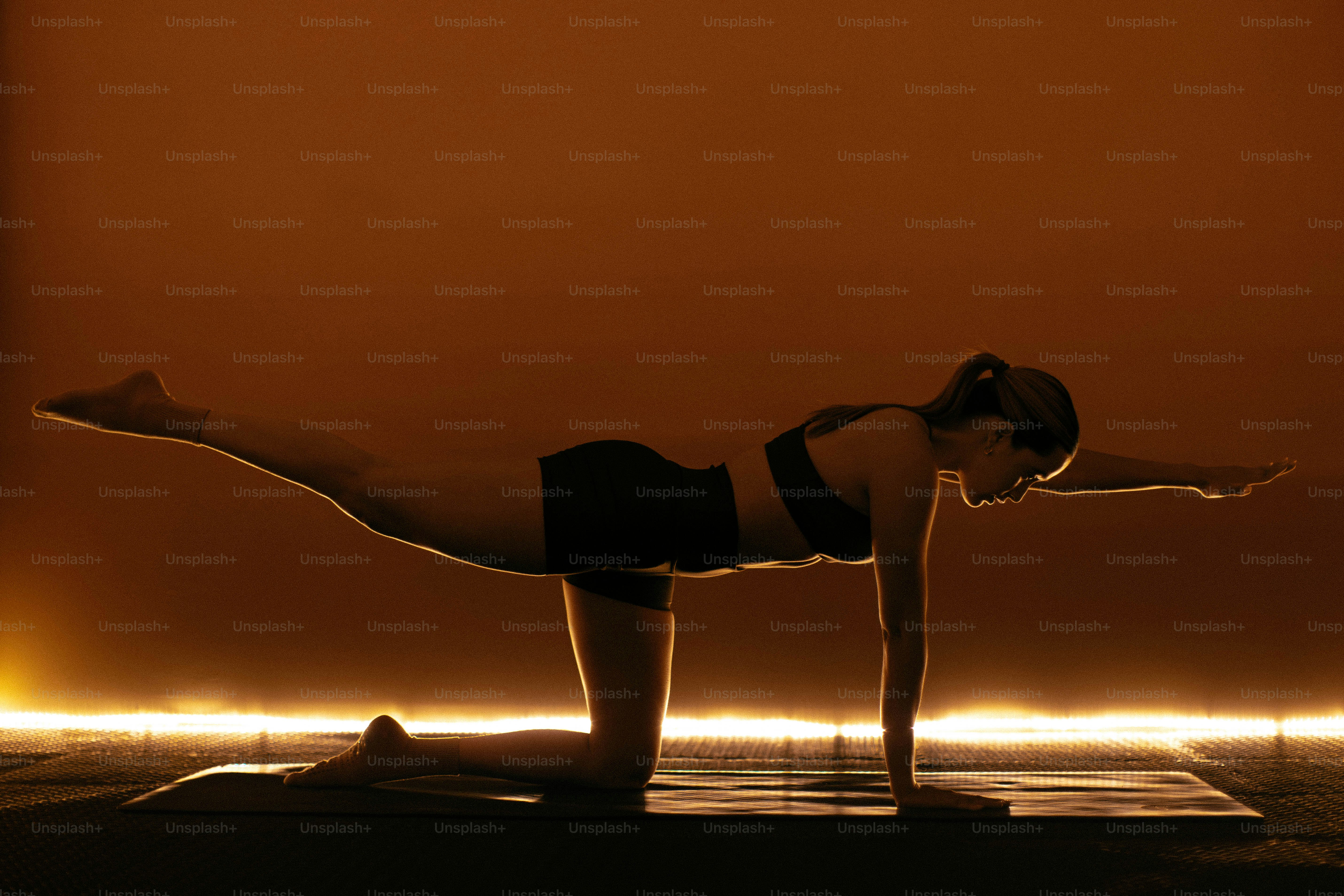 Una donna in posizione yoga contro un bagliore arancione.