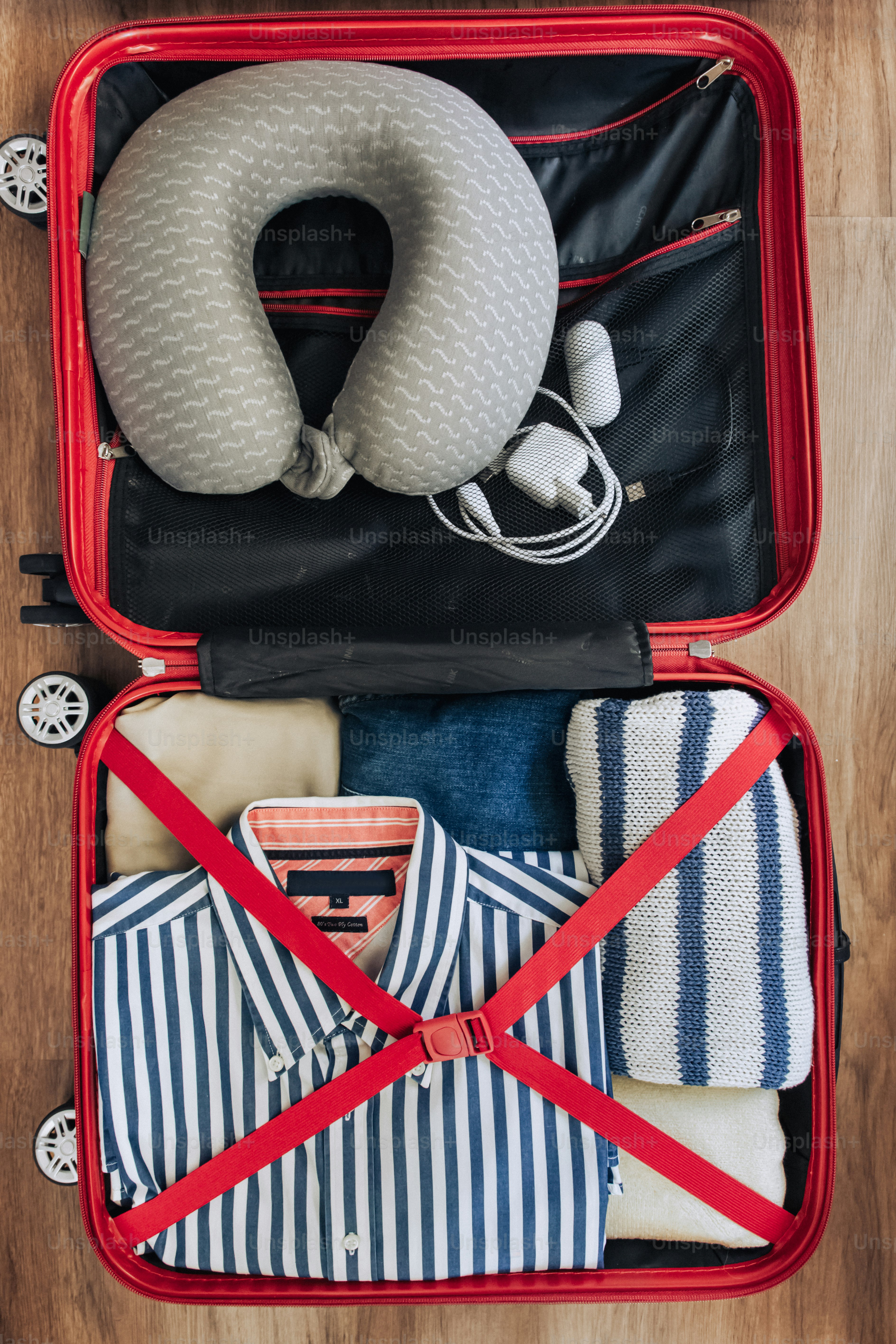 Valise rouge ouverte remplie de vêtements et d’oreiller pour le cou.