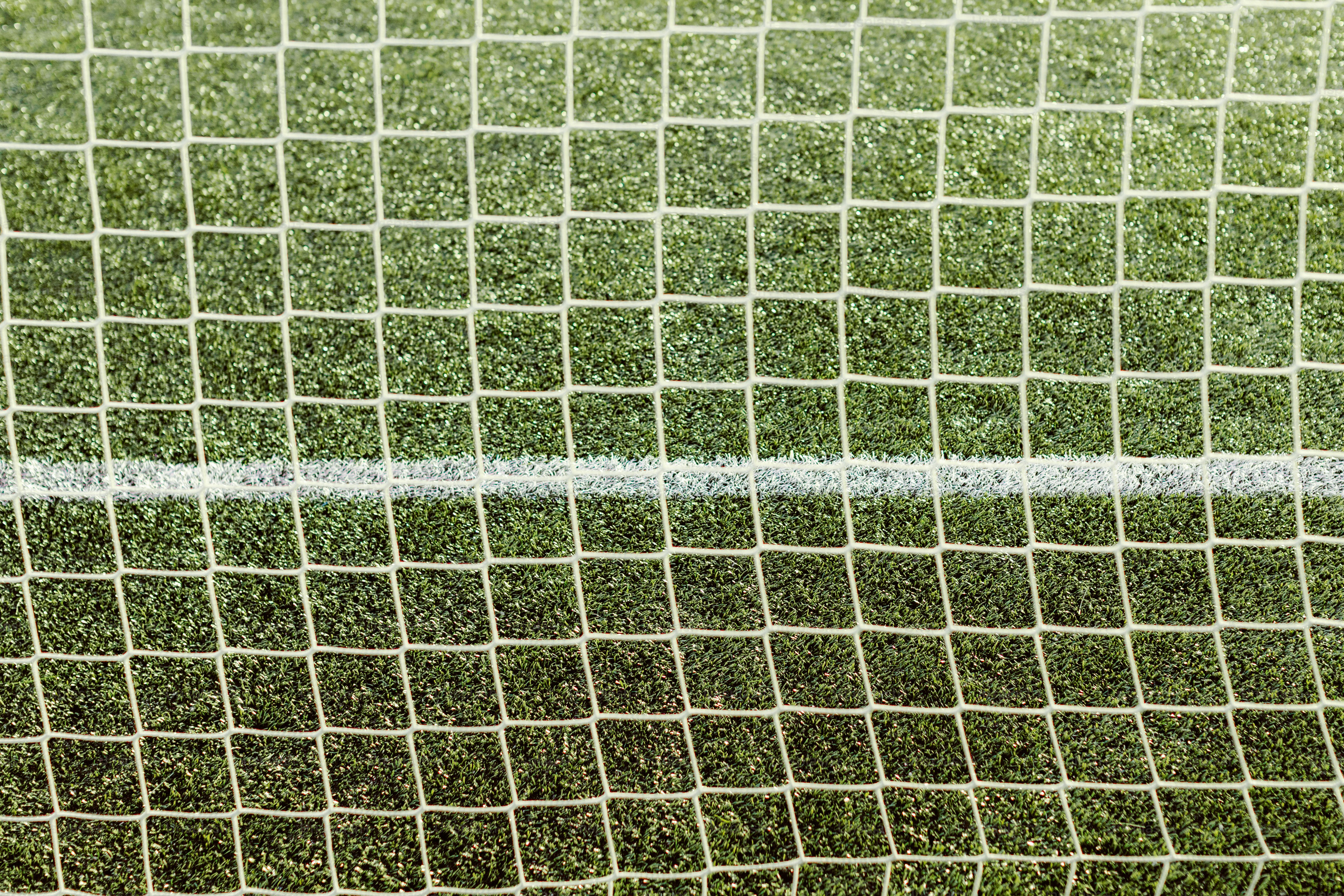 Jaring sepak bola dengan garis putih di atas rumput buatan hijau.