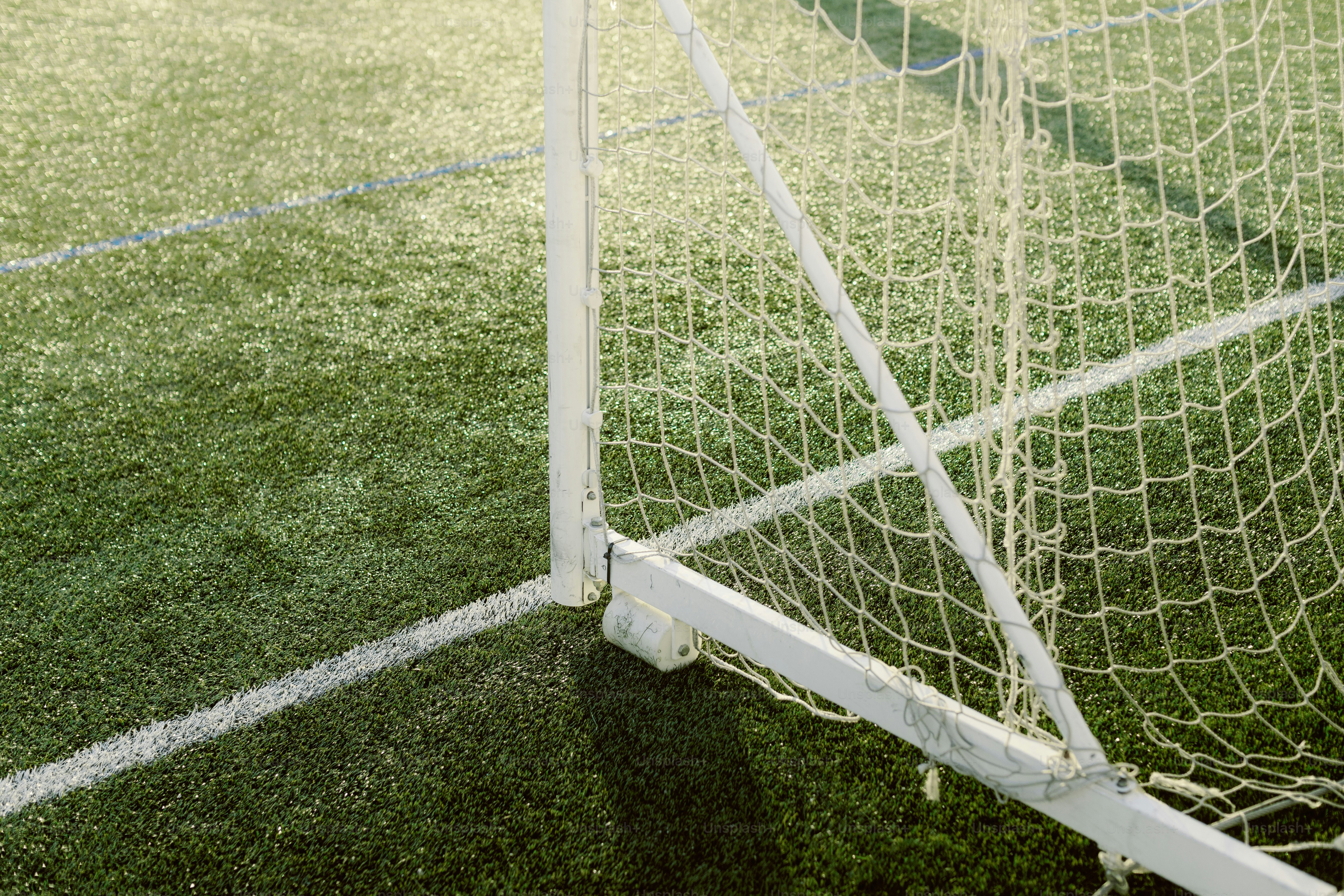 Close-up gawang sepak bola putih di lapangan hijau.