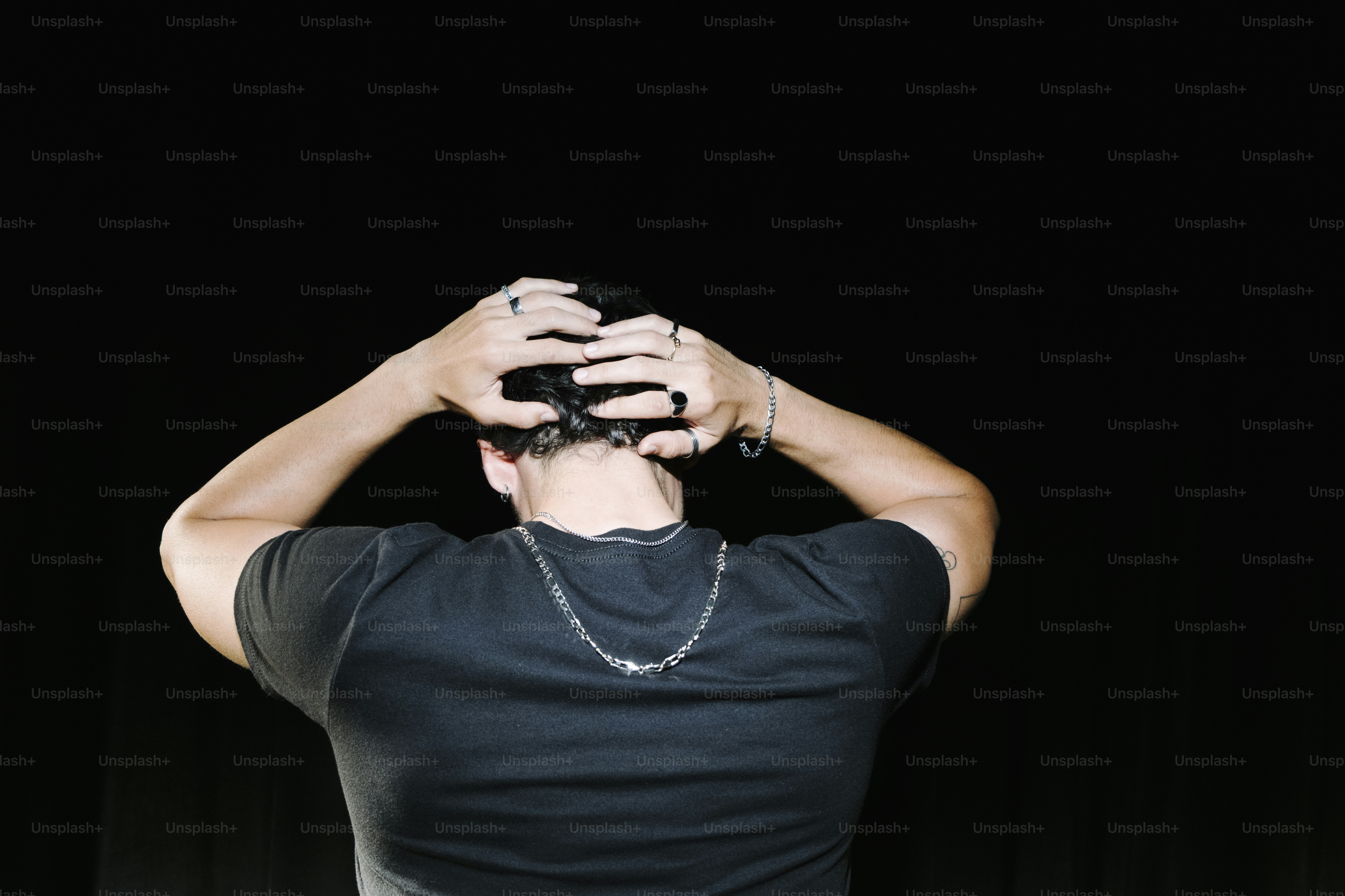 Man seen from behind with hands on head.