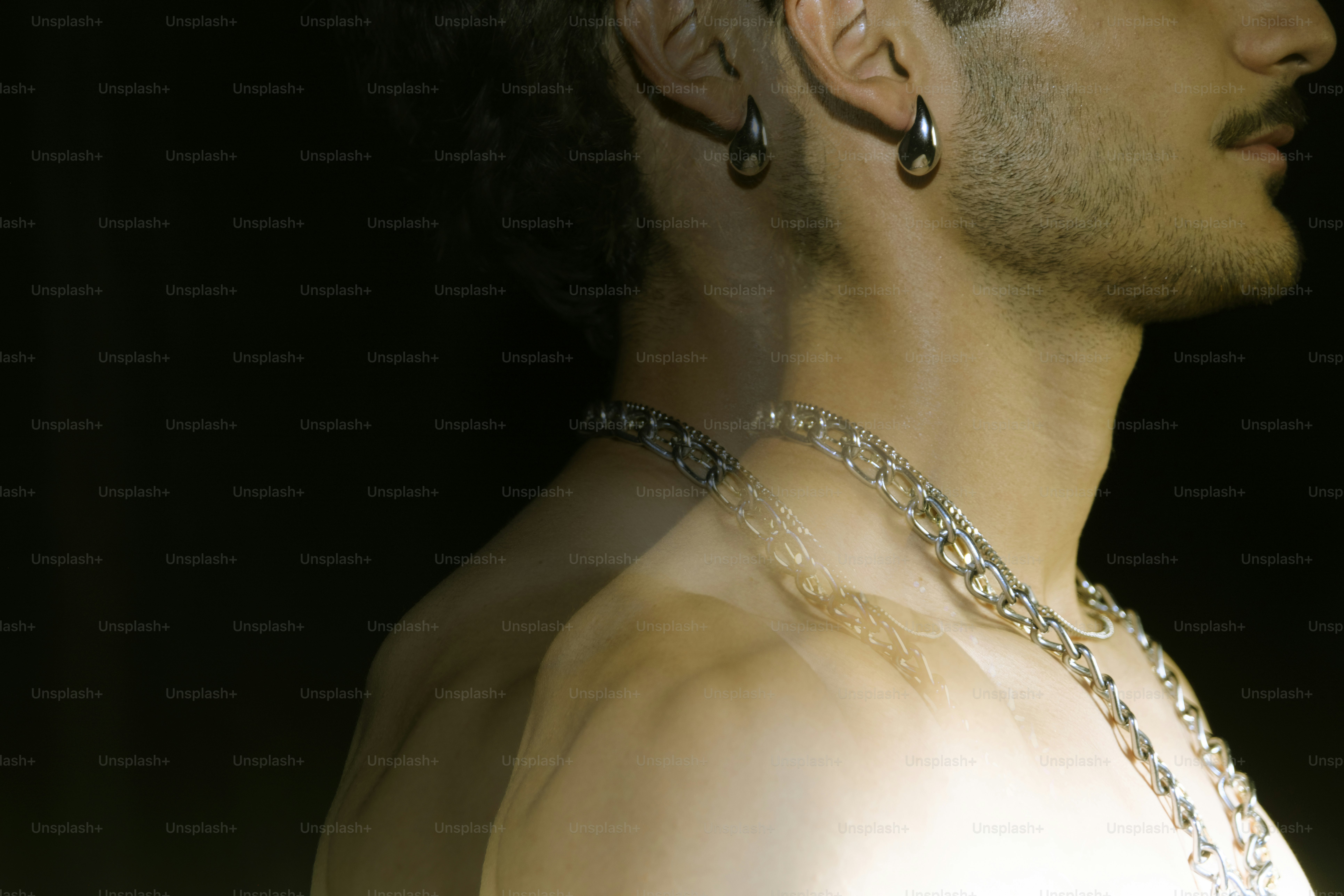Man with earrings and necklaces against dark background