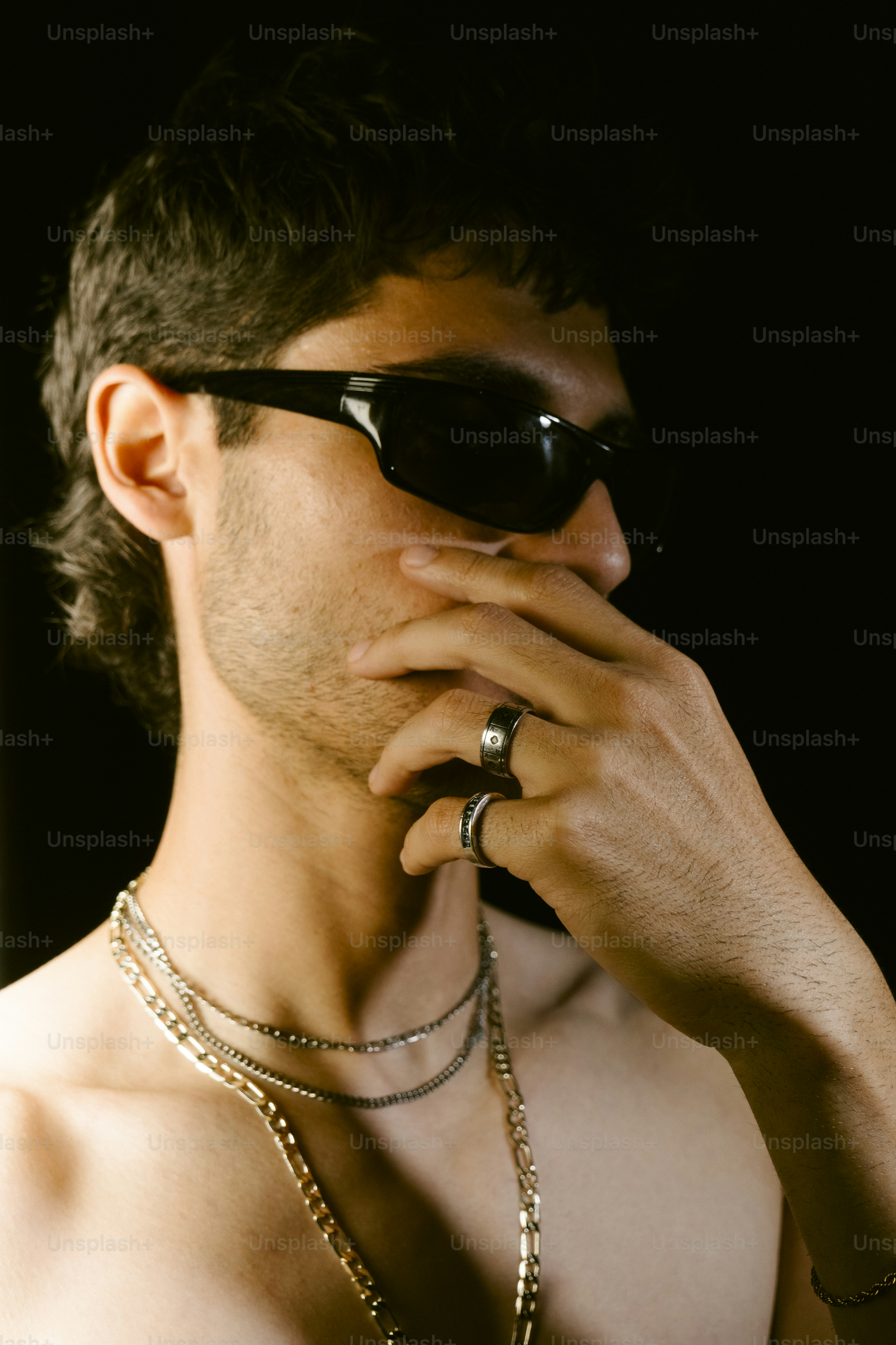 Man wearing sunglasses and jewelry against a black background