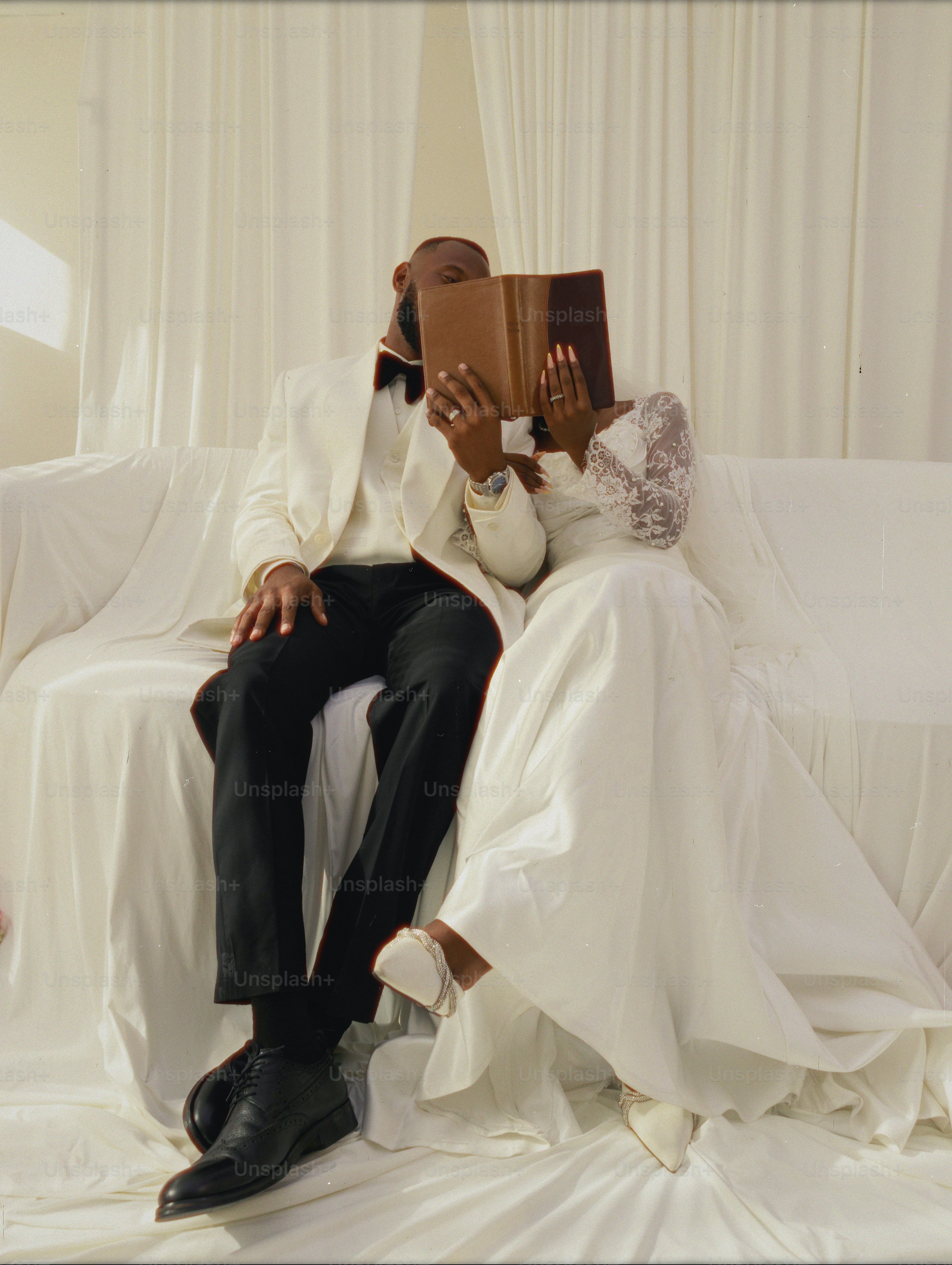 Couple in wedding attire reading a book on couch