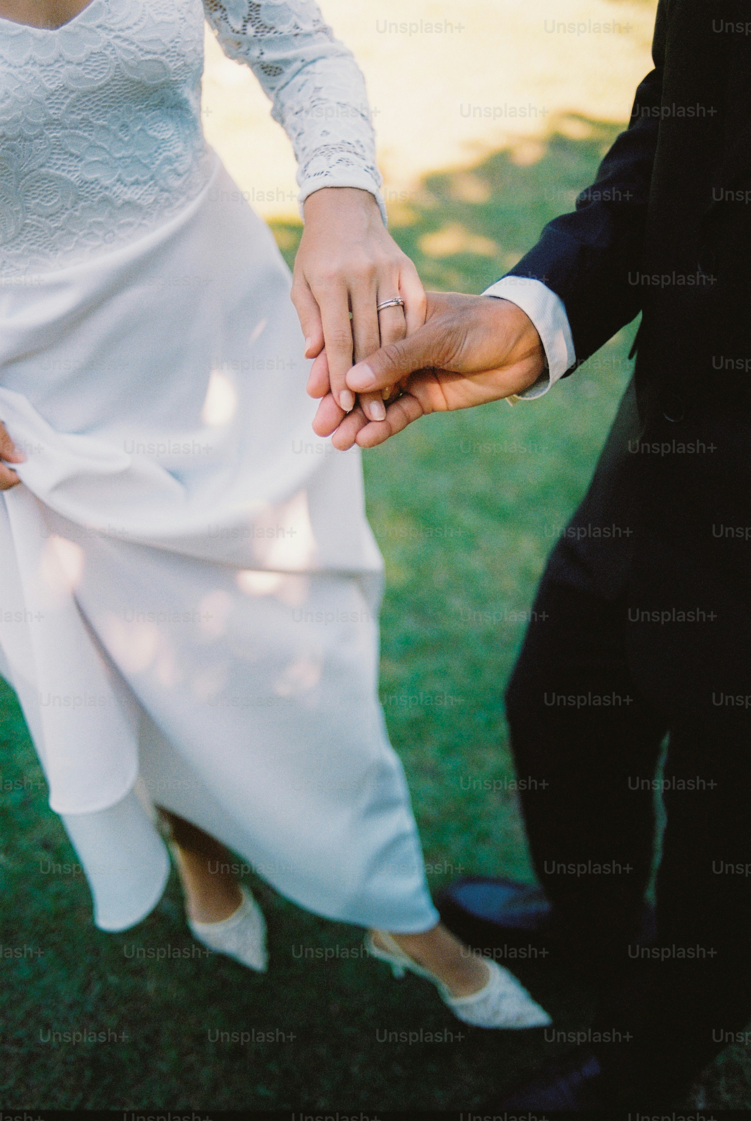 Pengantin baru berpegangan tangan, berjalan di atas rumput hijau.