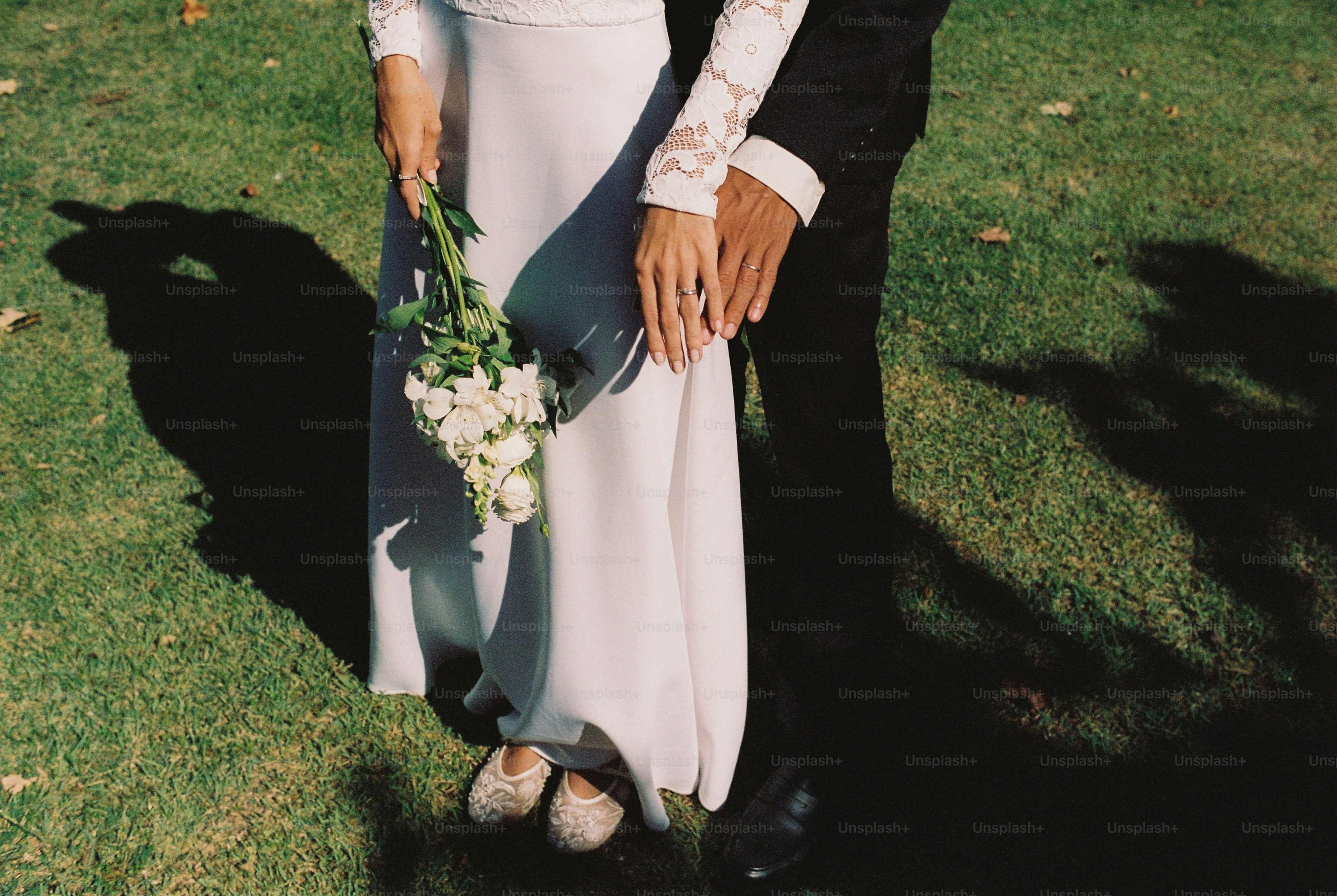 Pasangan pengantin berpegangan tangan dan buket bunga putih.