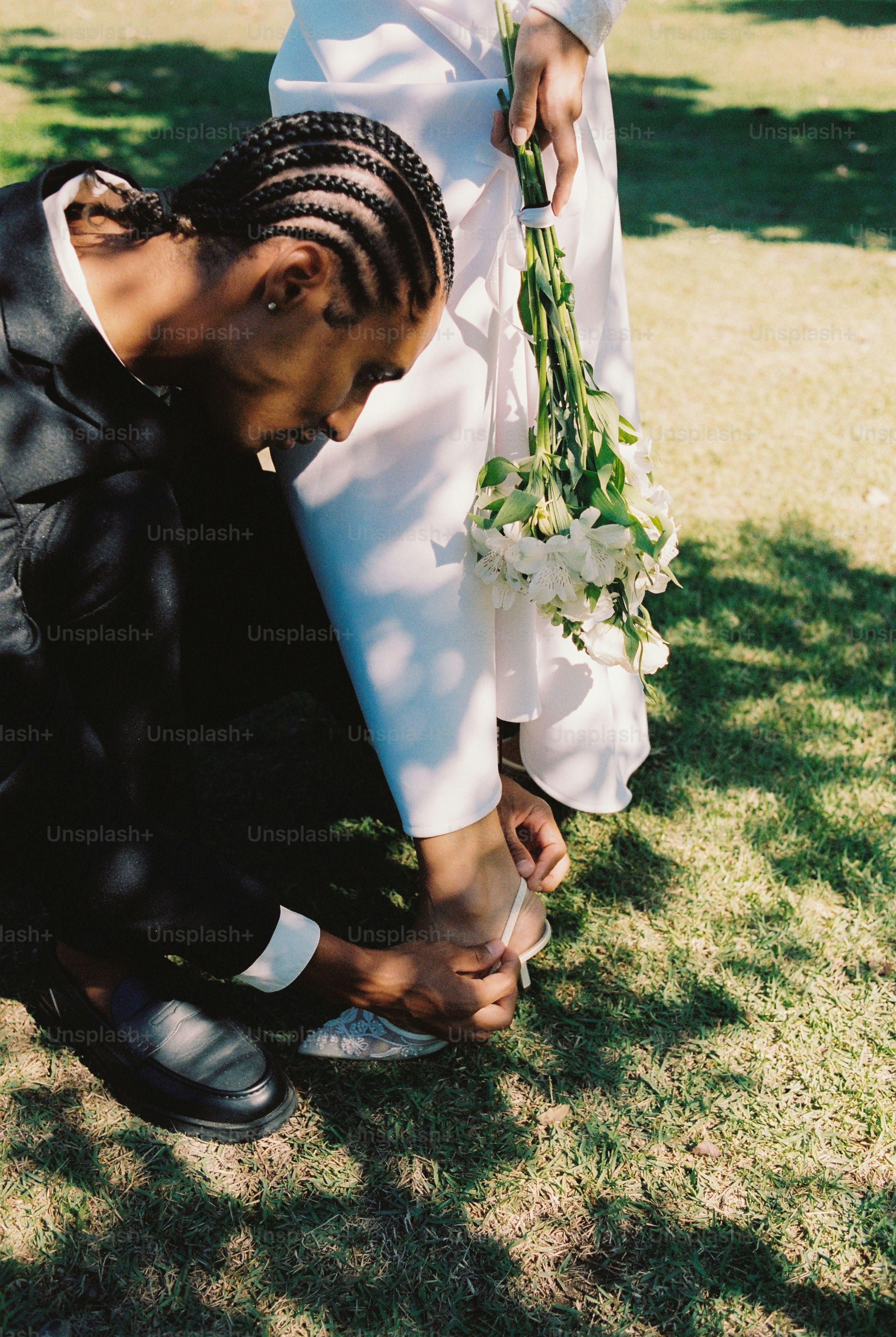 Pengantin pria mengikat sepatu pengantin wanita di halaman rumput
