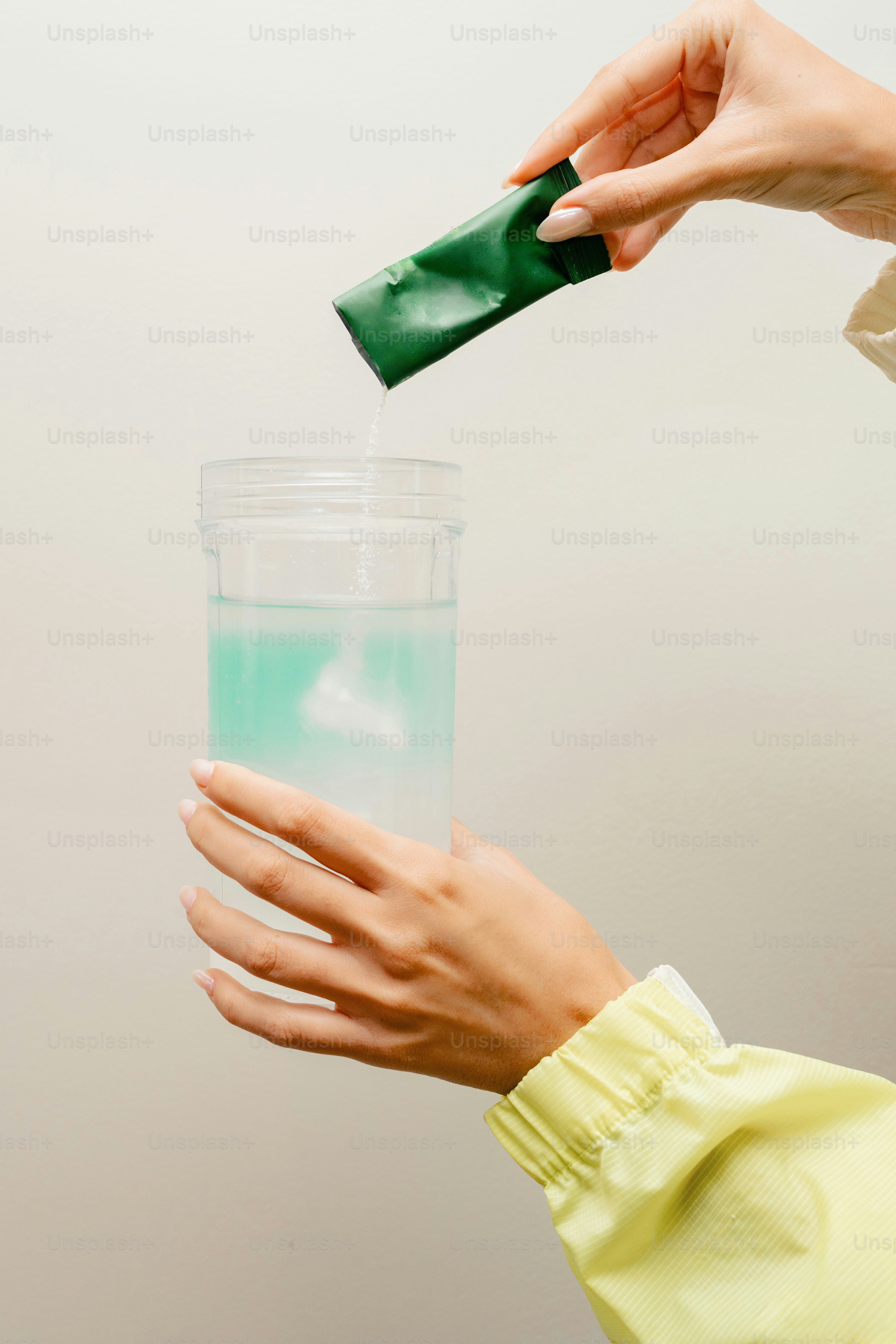 Hands pour green packet into a glass of blue liquid.