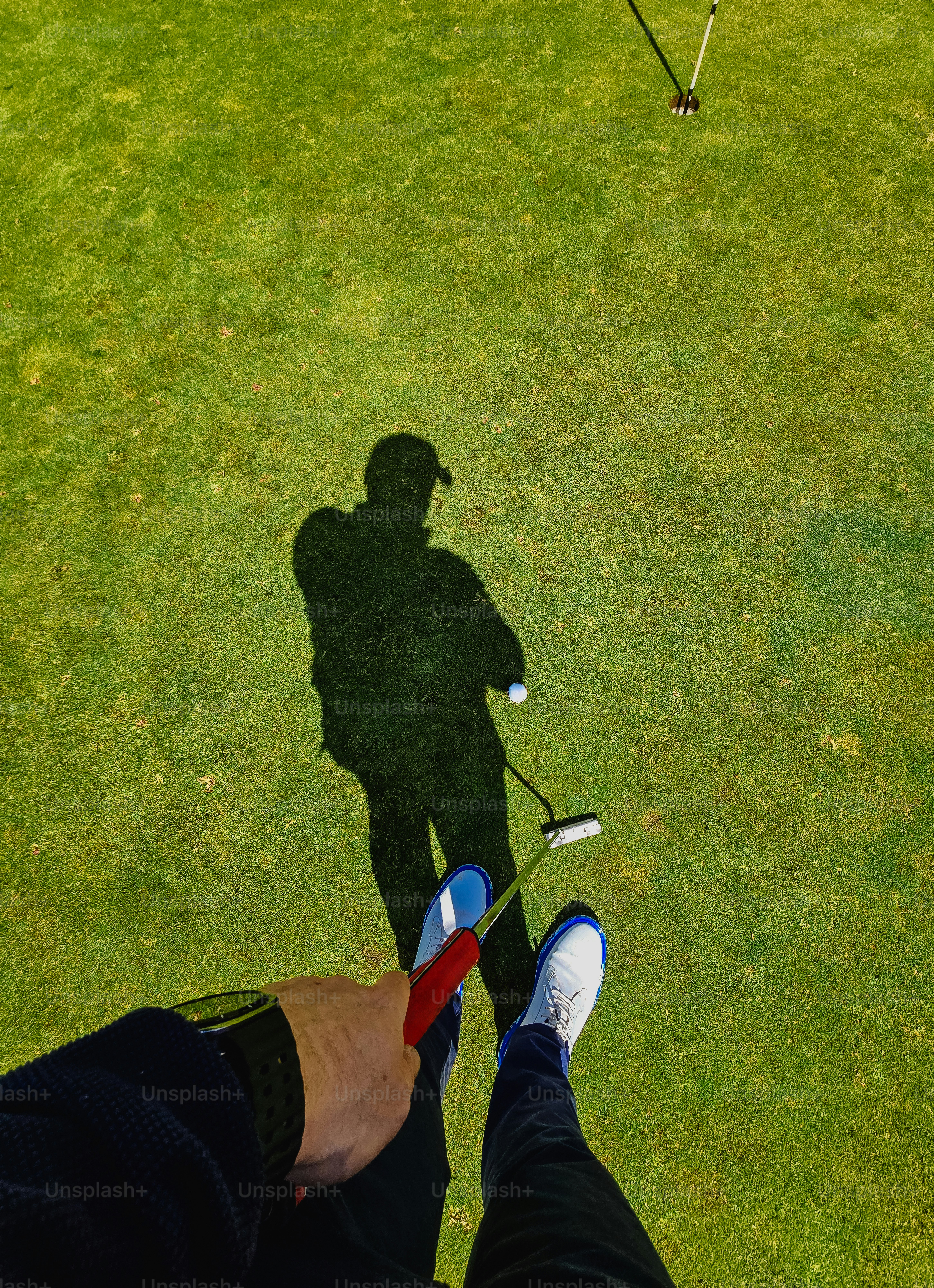 Golfer's shadow on a green golf course with a putter.