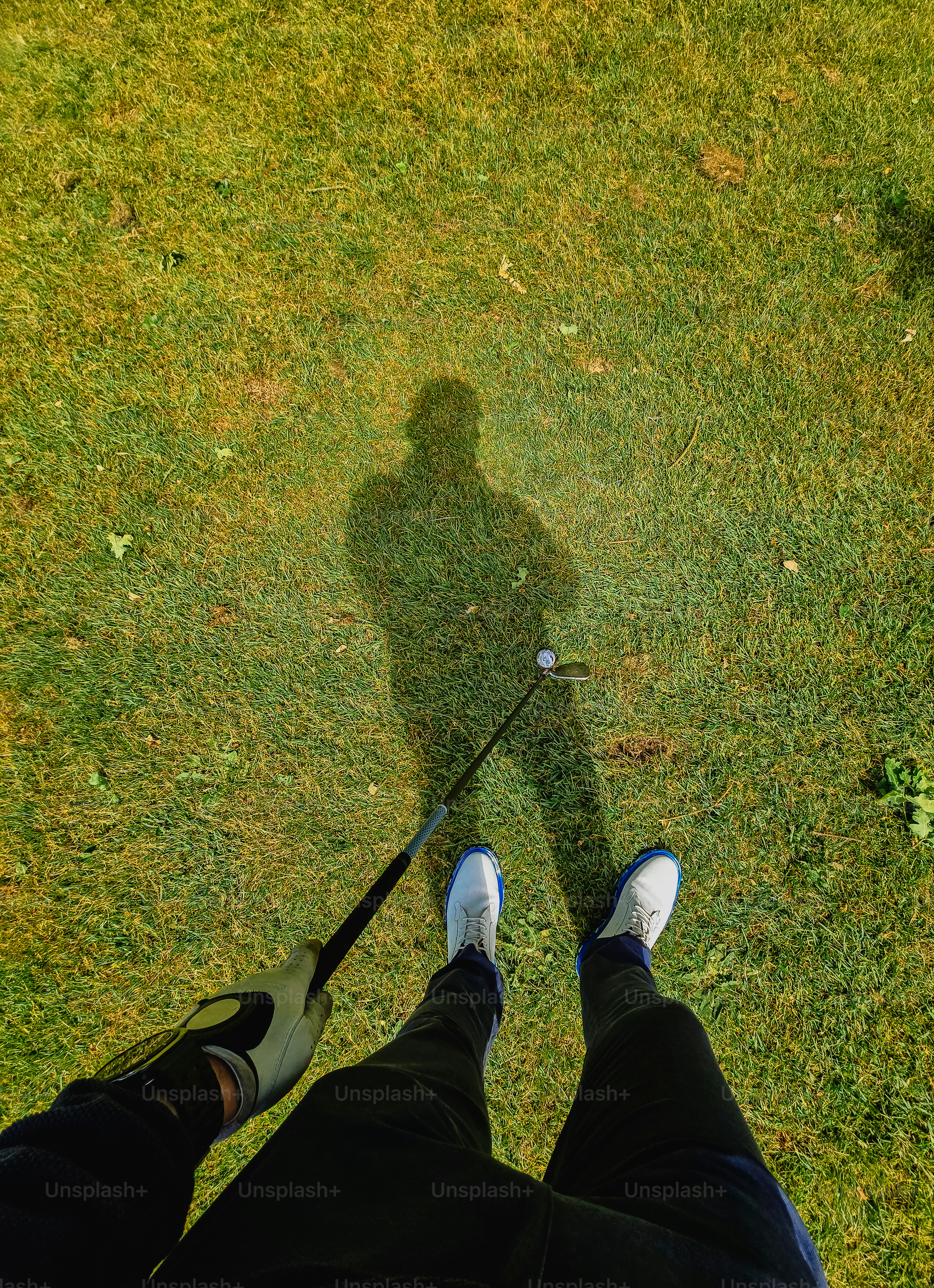 Golfer's perspective with shadow, club, and ball on green.