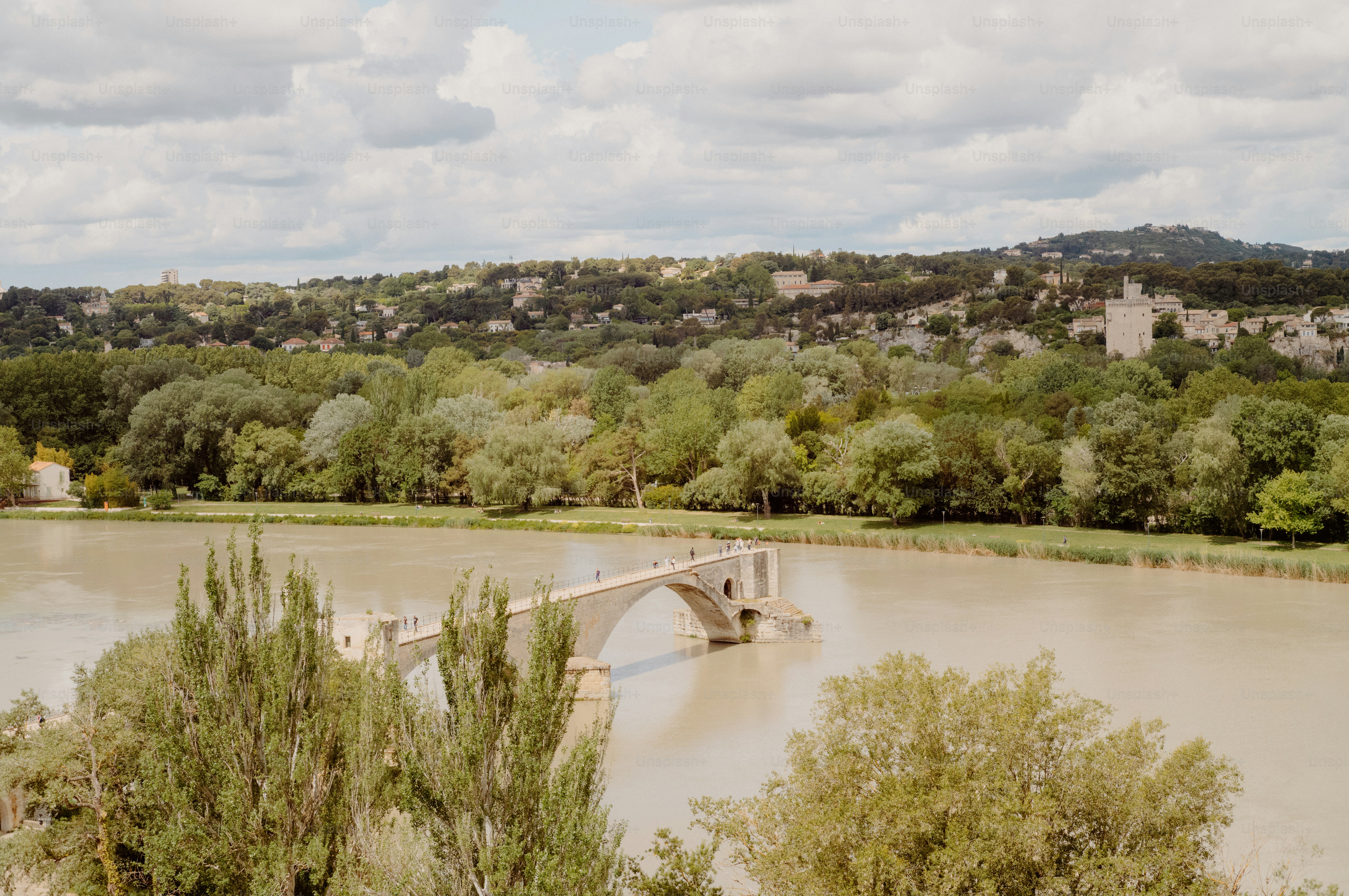 Stone bridge arches over a wide river with trees.