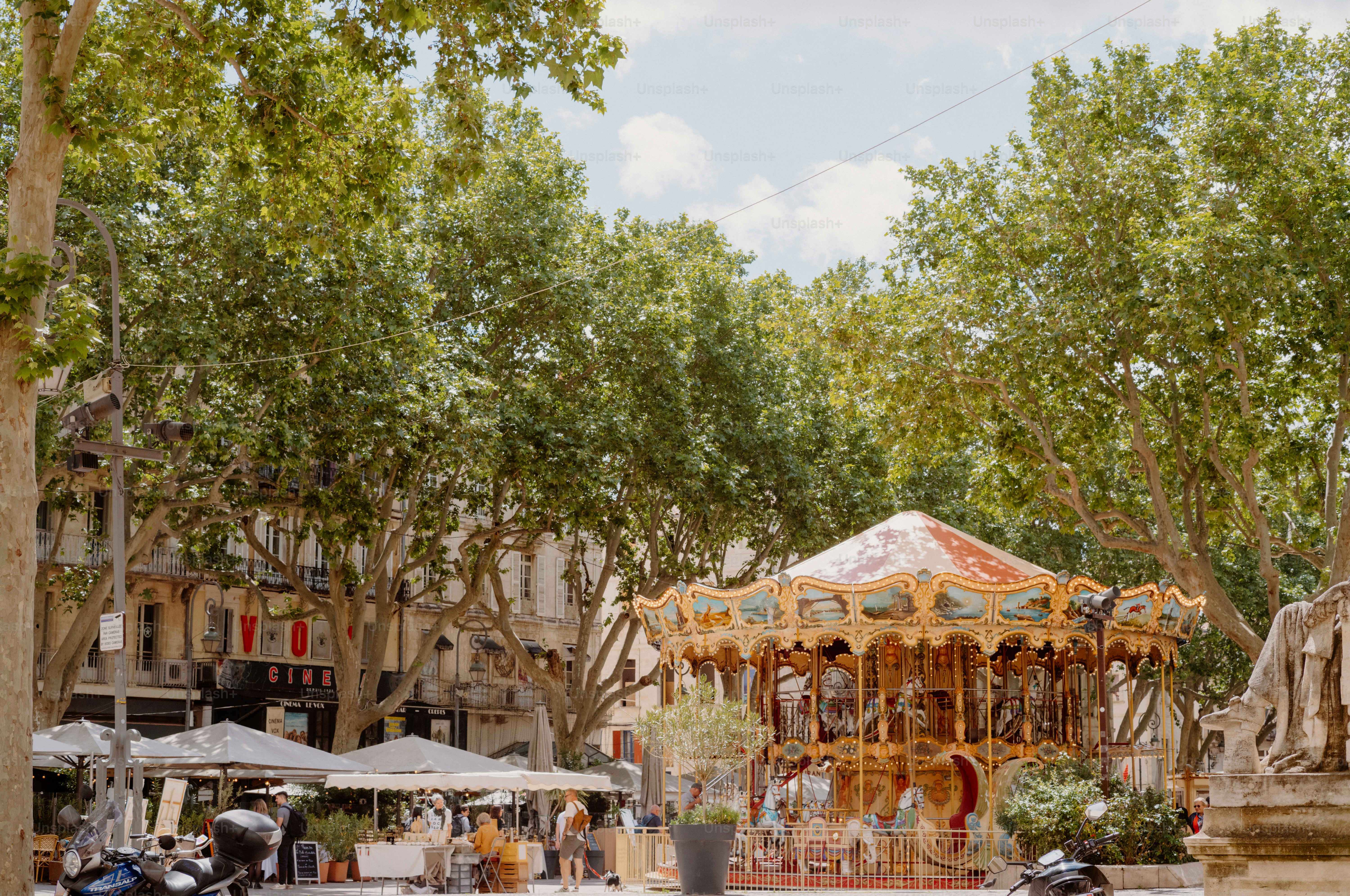 A vintage carousel in a town square under trees.