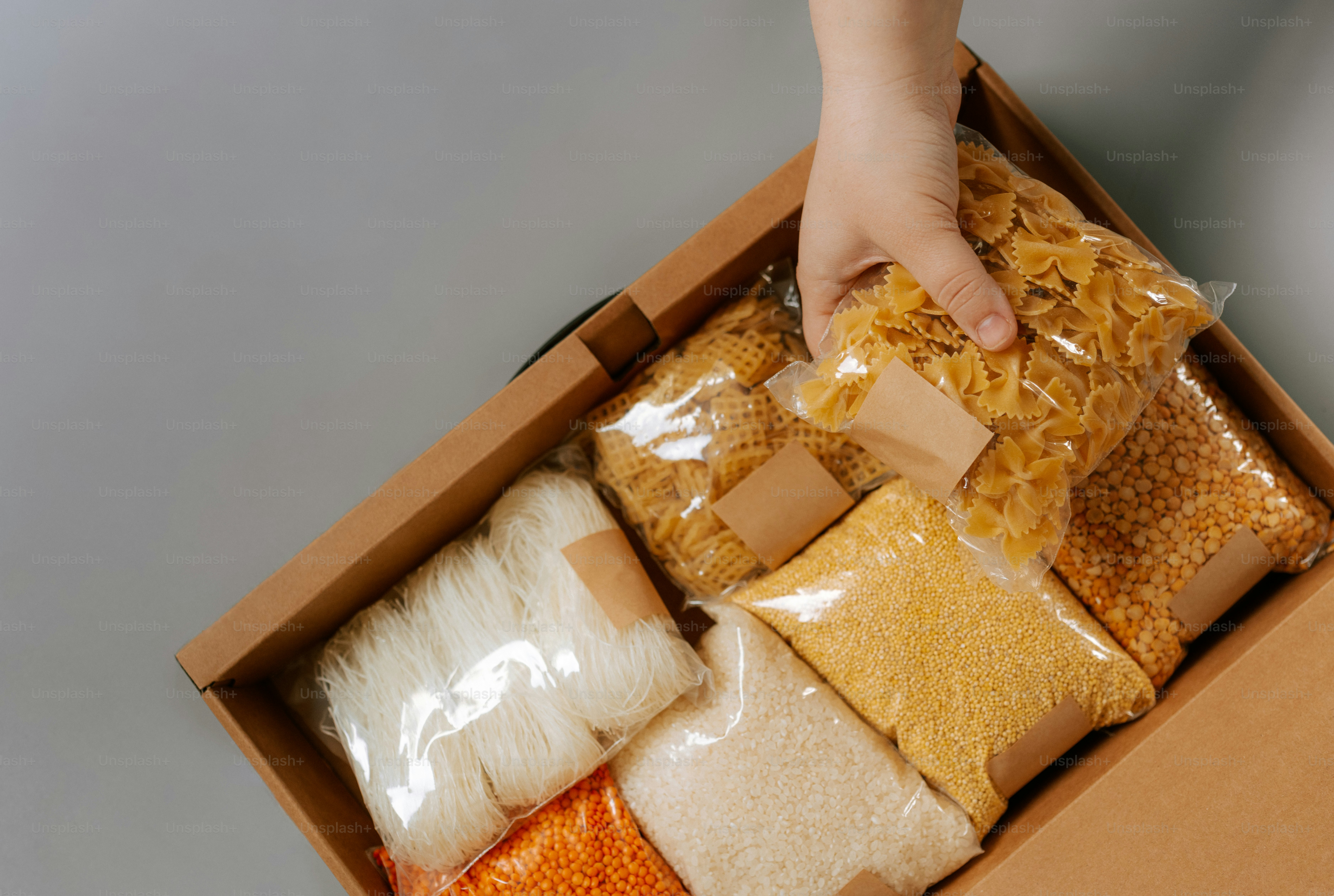 Una mano mette la pasta in una scatola di alimenti di base