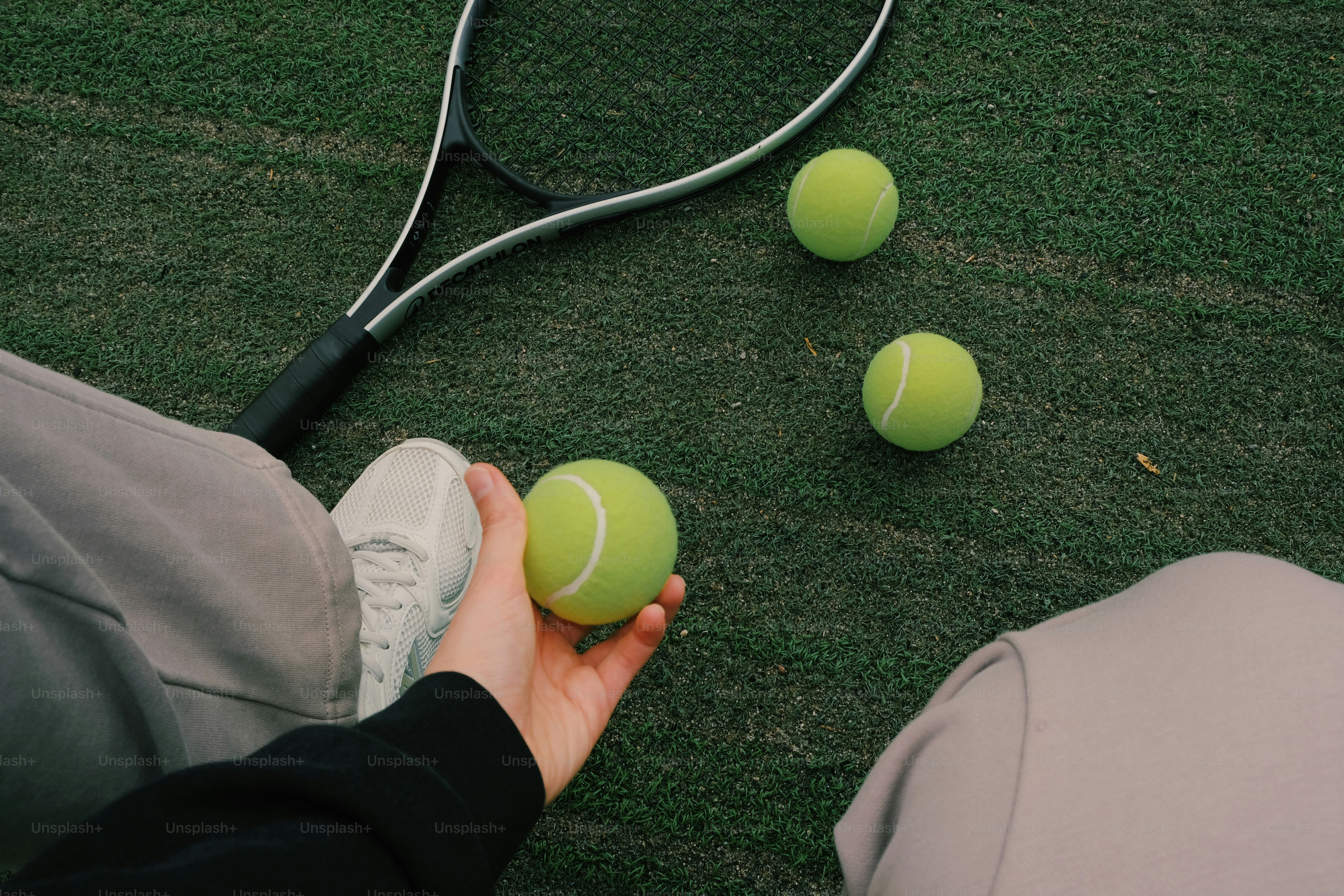 Una mano che tiene una pallina da tennis, una racchetta e due palle