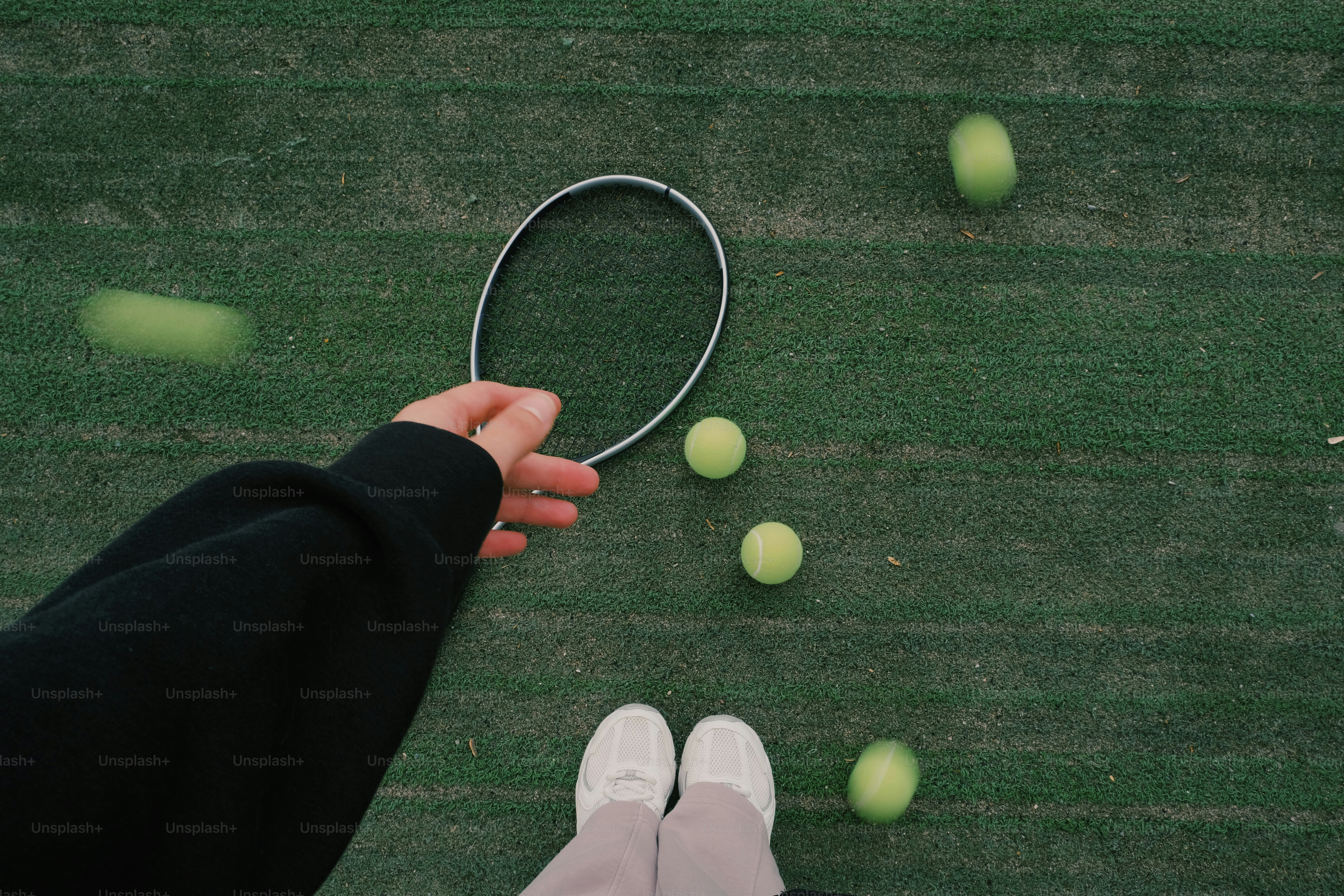 Persona che tiene una racchetta da tennis su un campo verde con palline sfocate