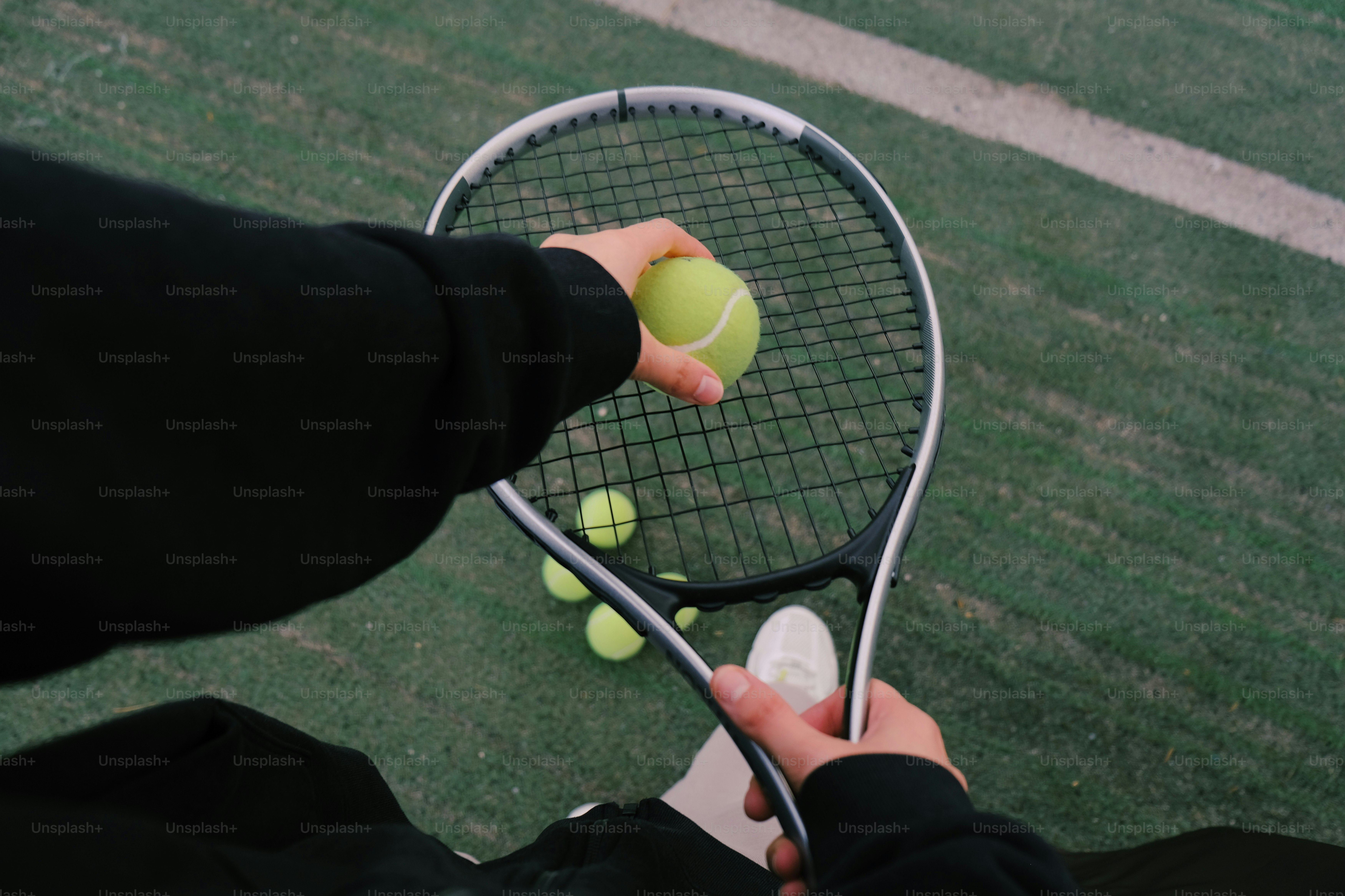 Mani che tengono racchetta da tennis e palla sul campo verde