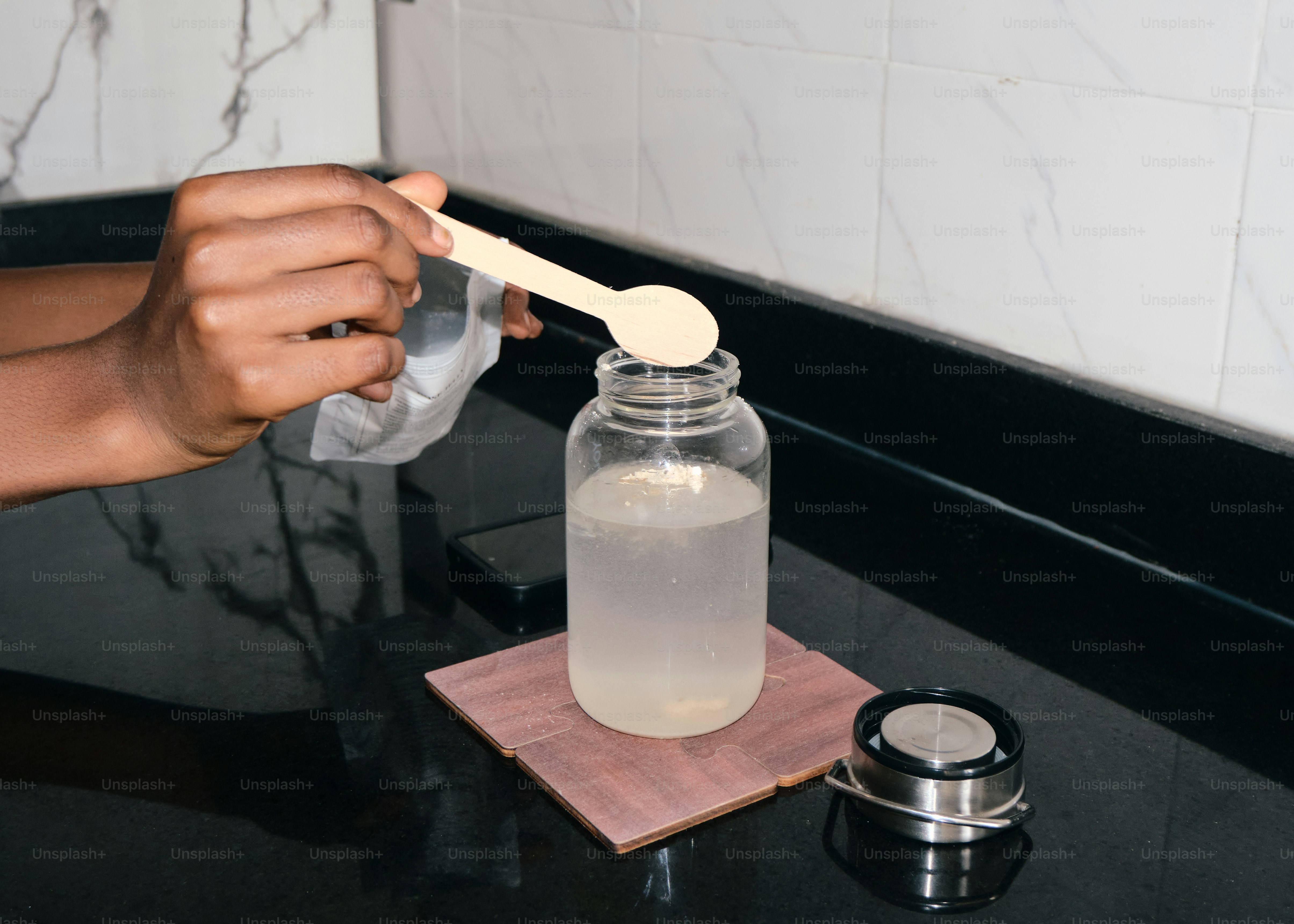 Mani che aggiungono polvere al liquido in una bottiglia trasparente.