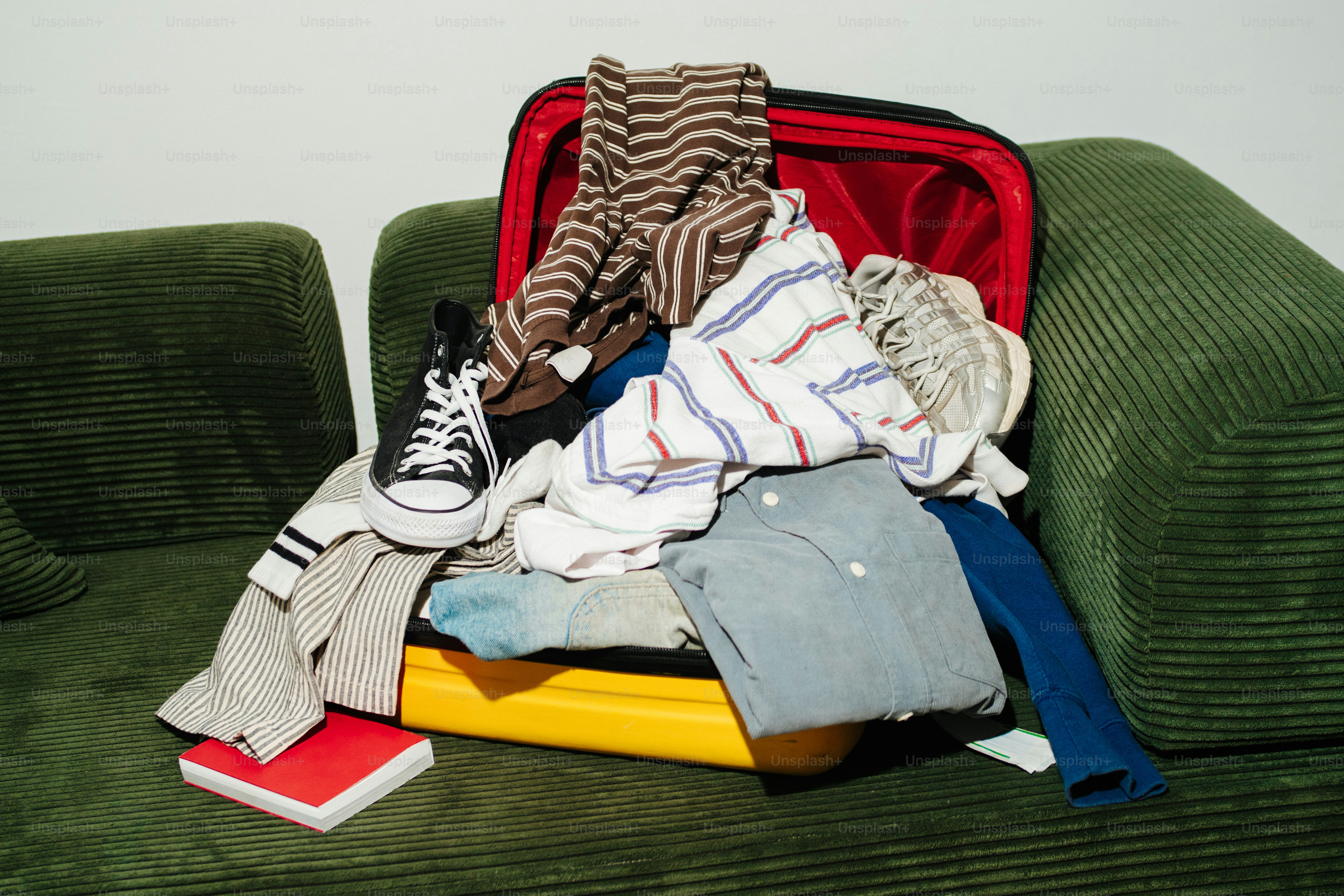 Übervollgepackter Koffer mit Kleidung und einem Sneaker auf einer Couch.