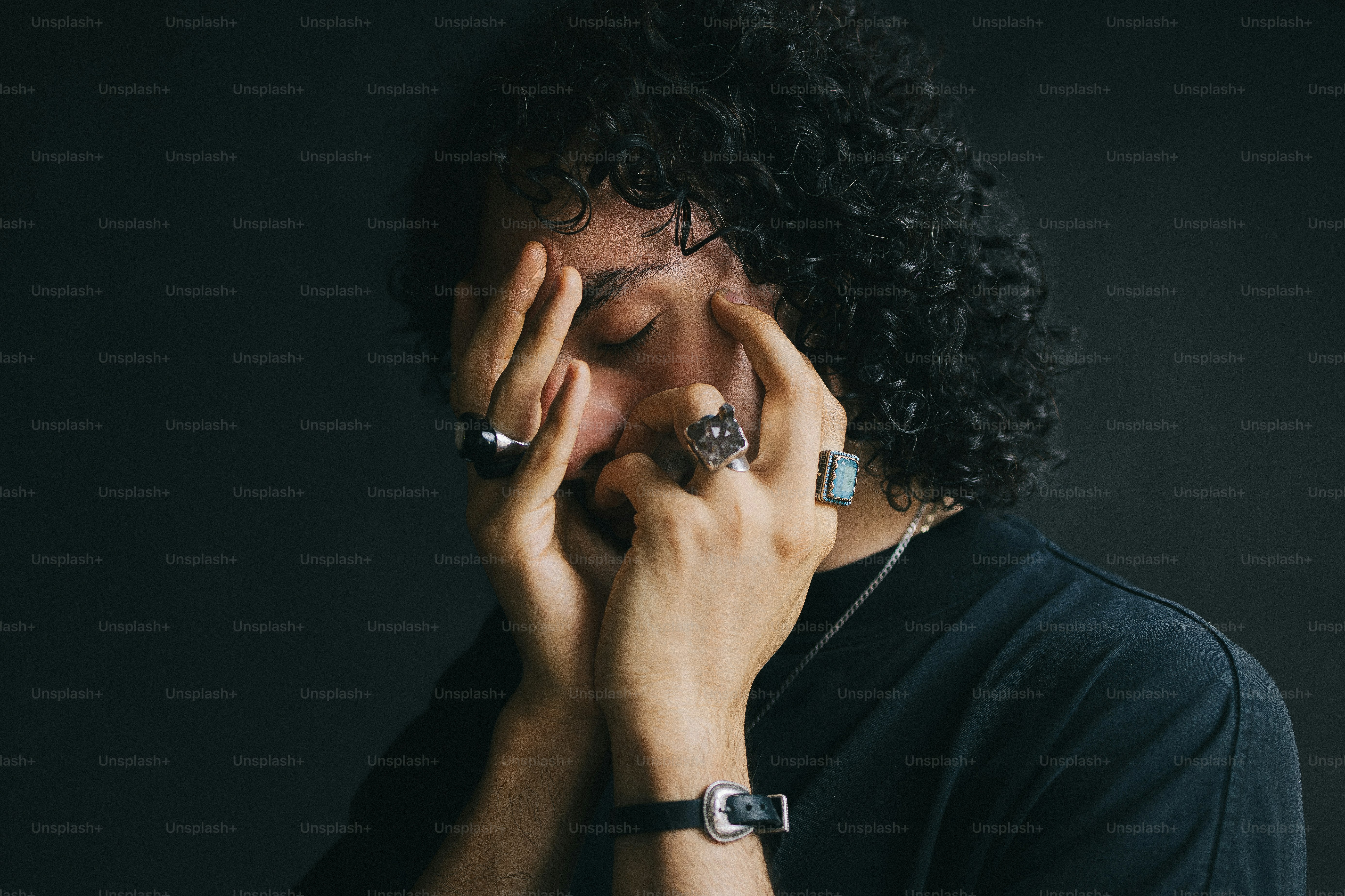 巻き毛の人が指輪をはめて顔を手で覆っている。